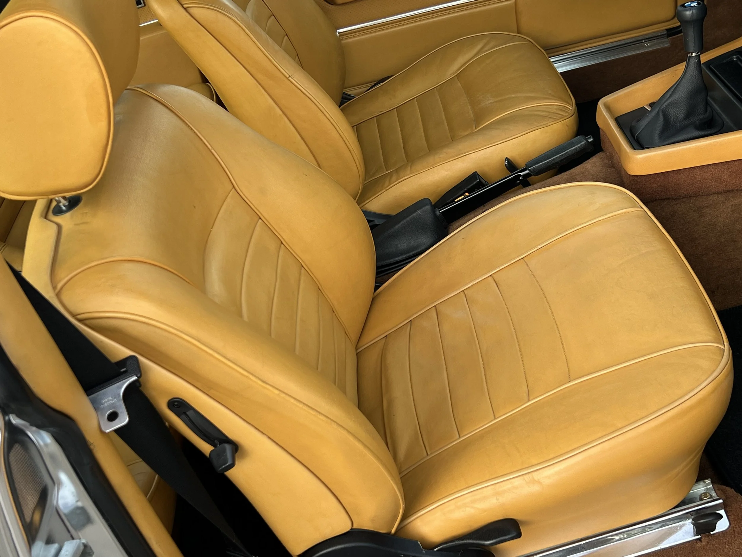 Close-up of two tan leather car seats with a manual gear shift in a vintage BMW 630 csi.