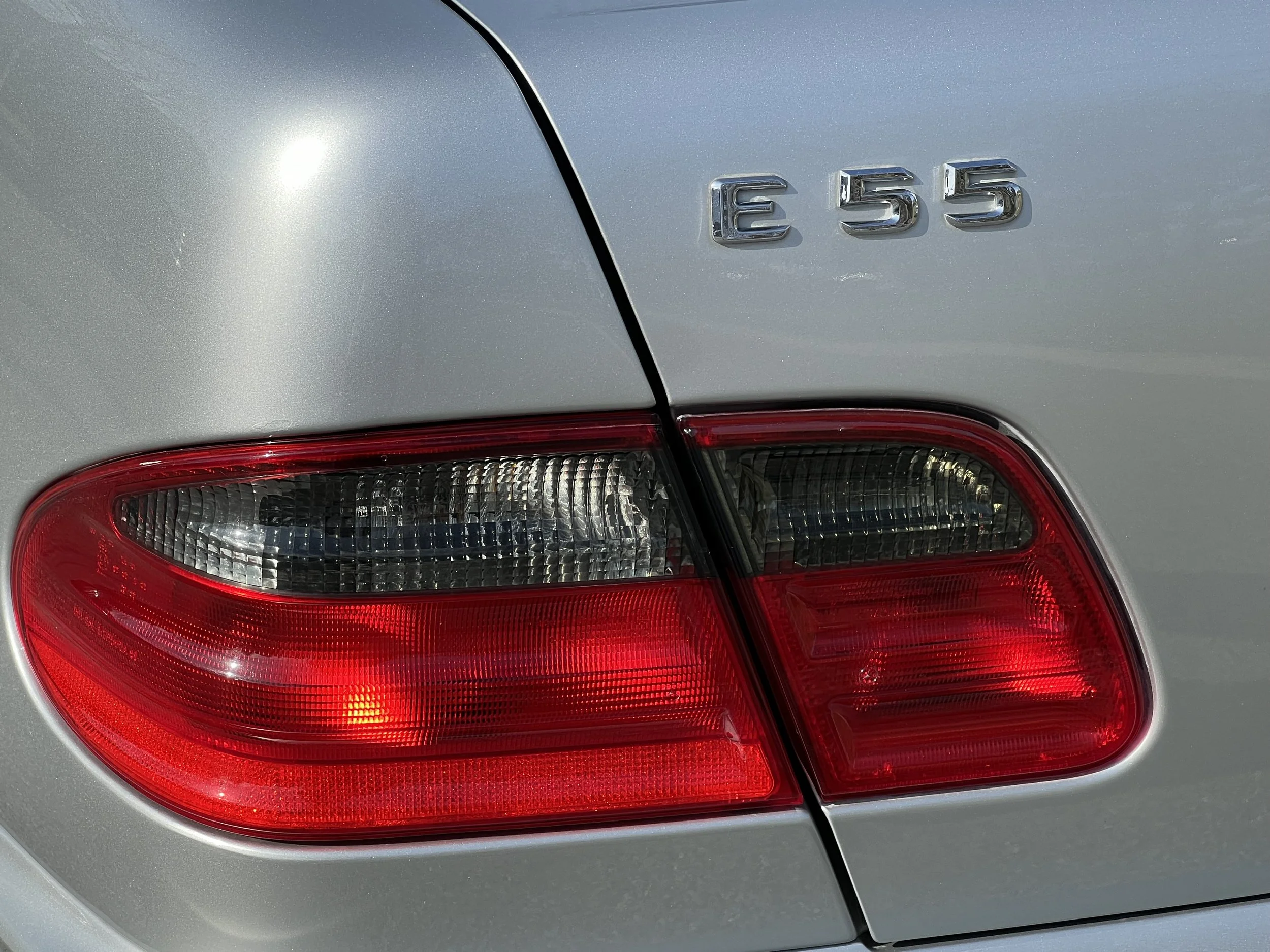 Close-up of the rear end of a silver Mercedes-Benz E55 car showing the tail light and the model badge.