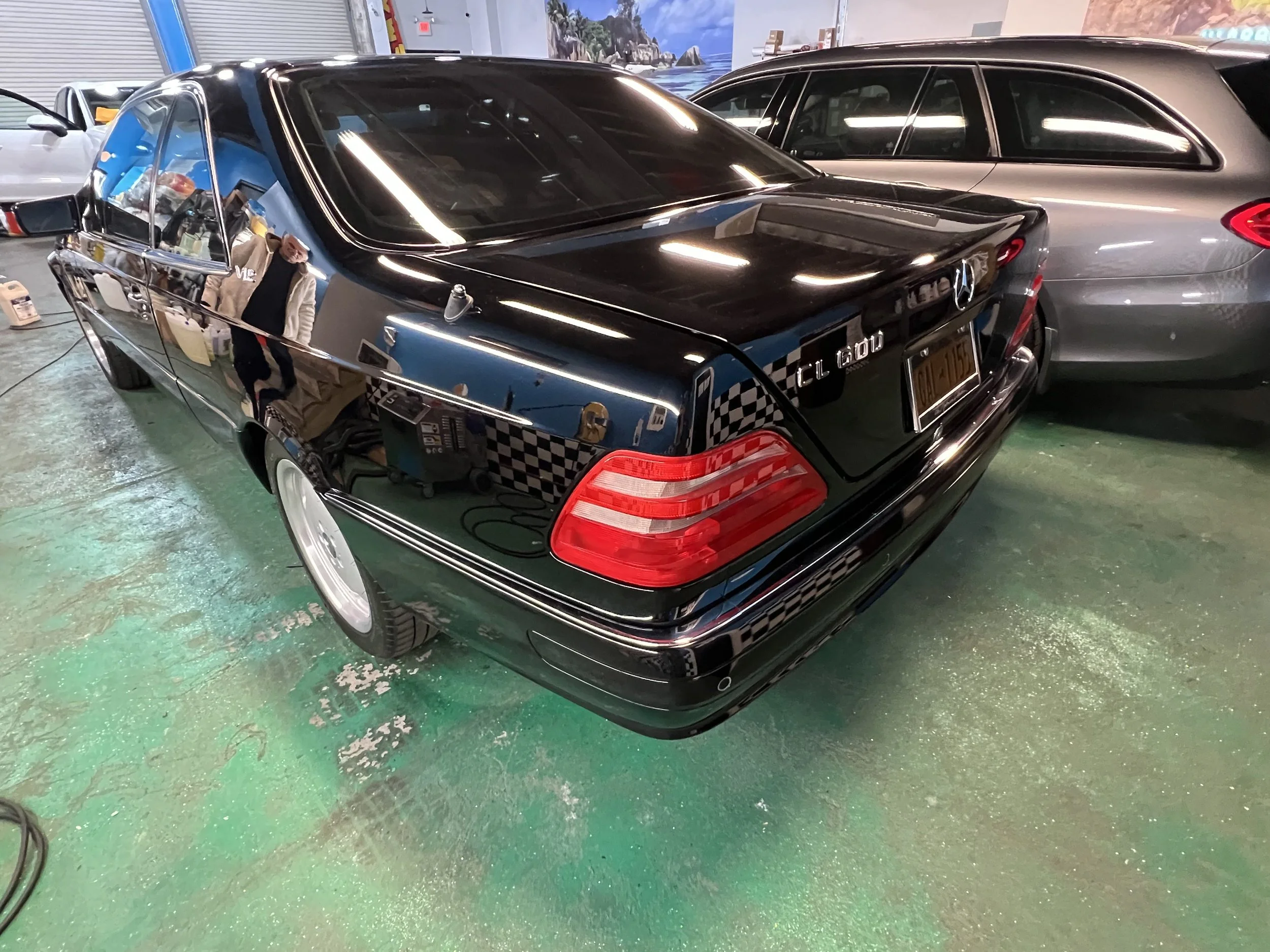 A black Mercedes-Benz CL 600 with a shiny, reflective surface parked indoors next to a gray car.