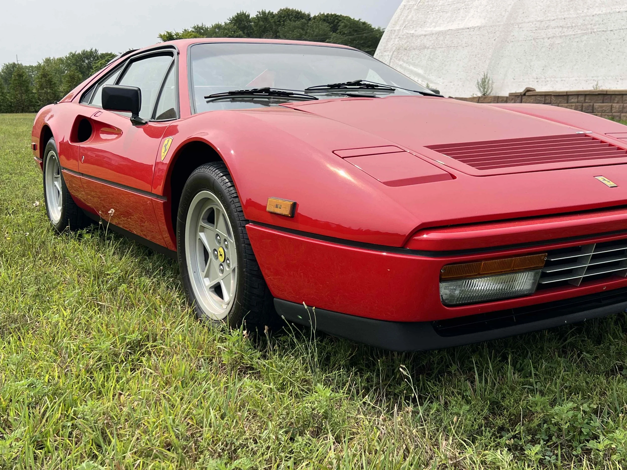 Red vintage Ferrari sports car parked on grass with a white building and trees in the background.