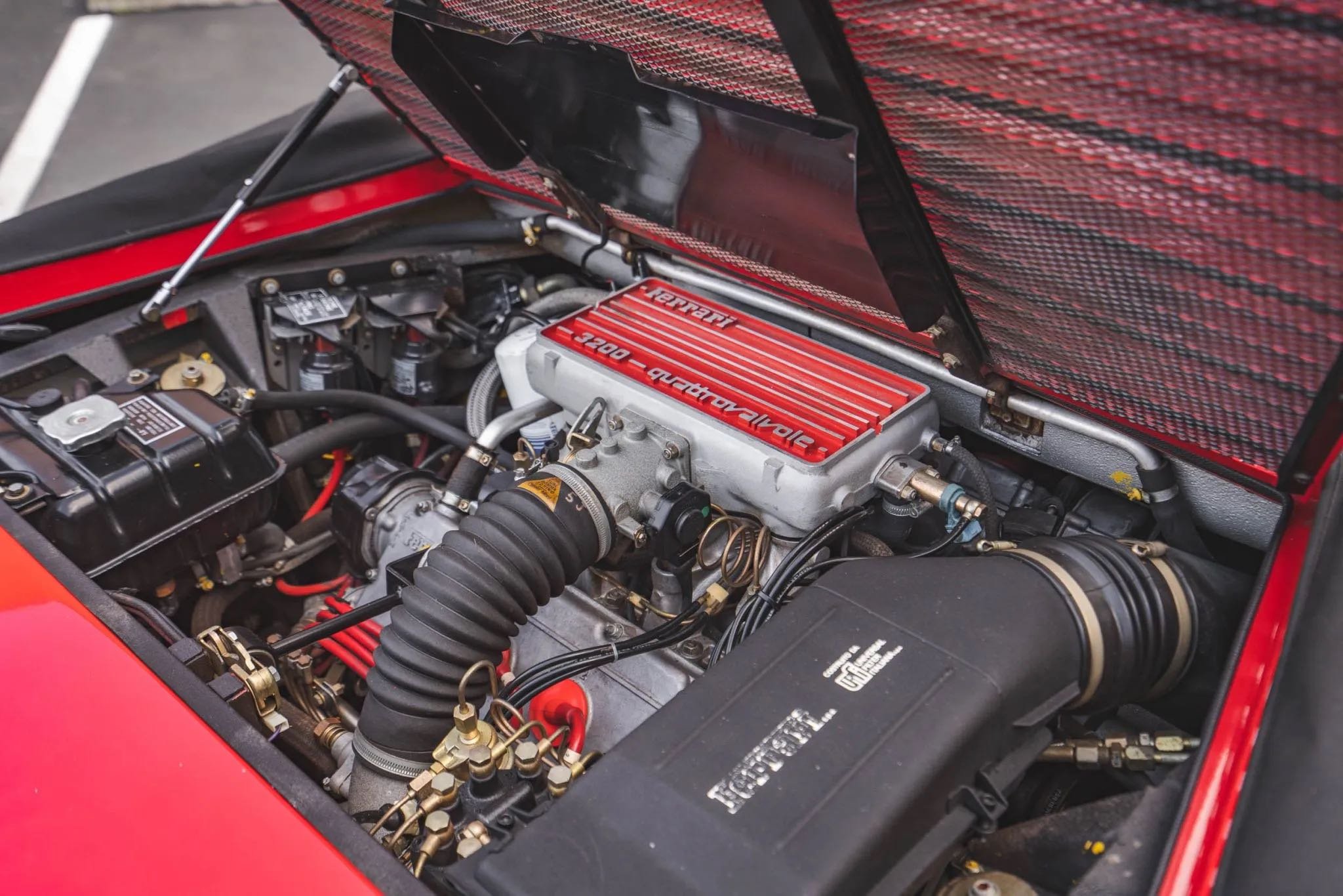 Close-up of a Ferrari Formula 1 car engine with a red, silver, and black color scheme, showing various mechanical components and hoses.