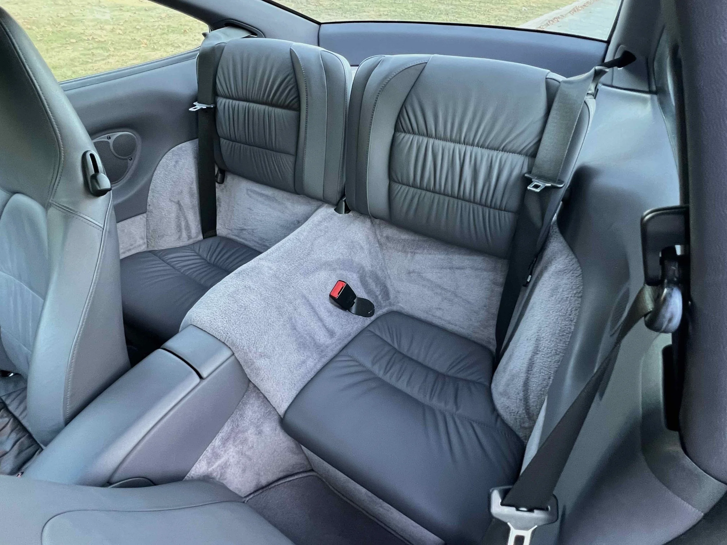 The back seats of a car with gray leather upholstery and gray fabric carpeting.