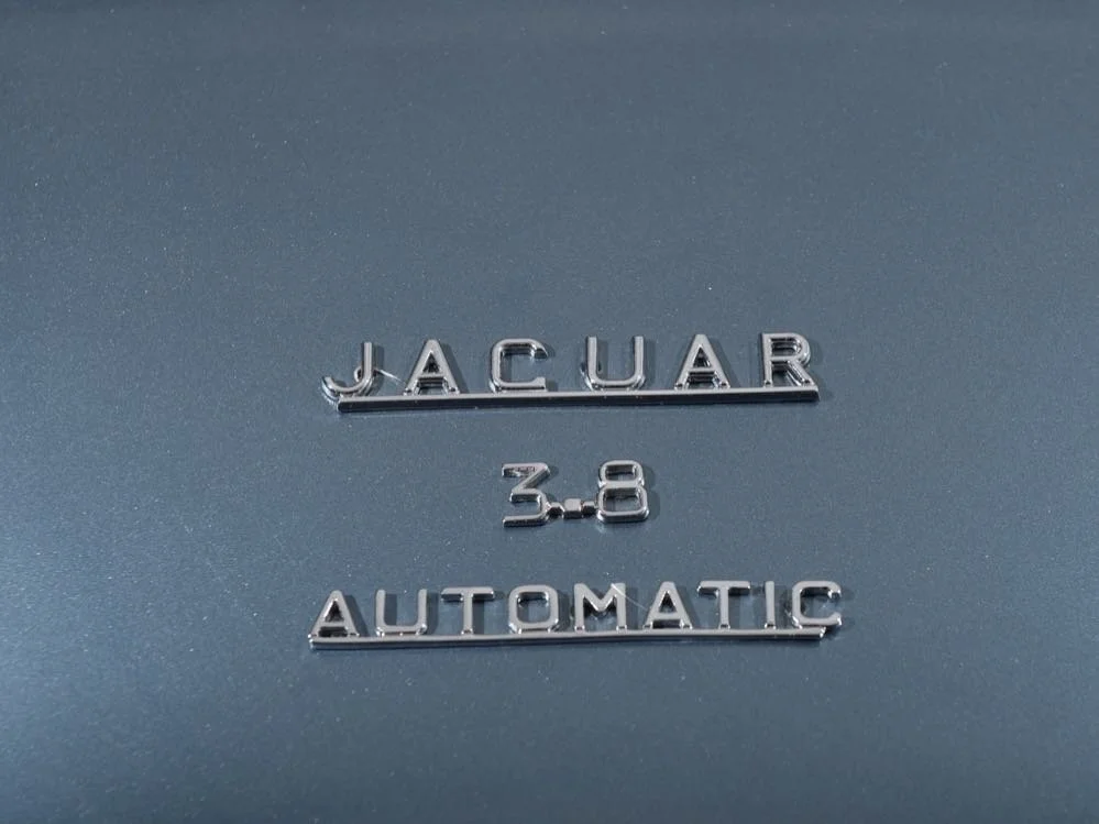 Close-up of a metallic badge on a vehicle, reading "JAGUAR 3.8 AUTOMATIC."