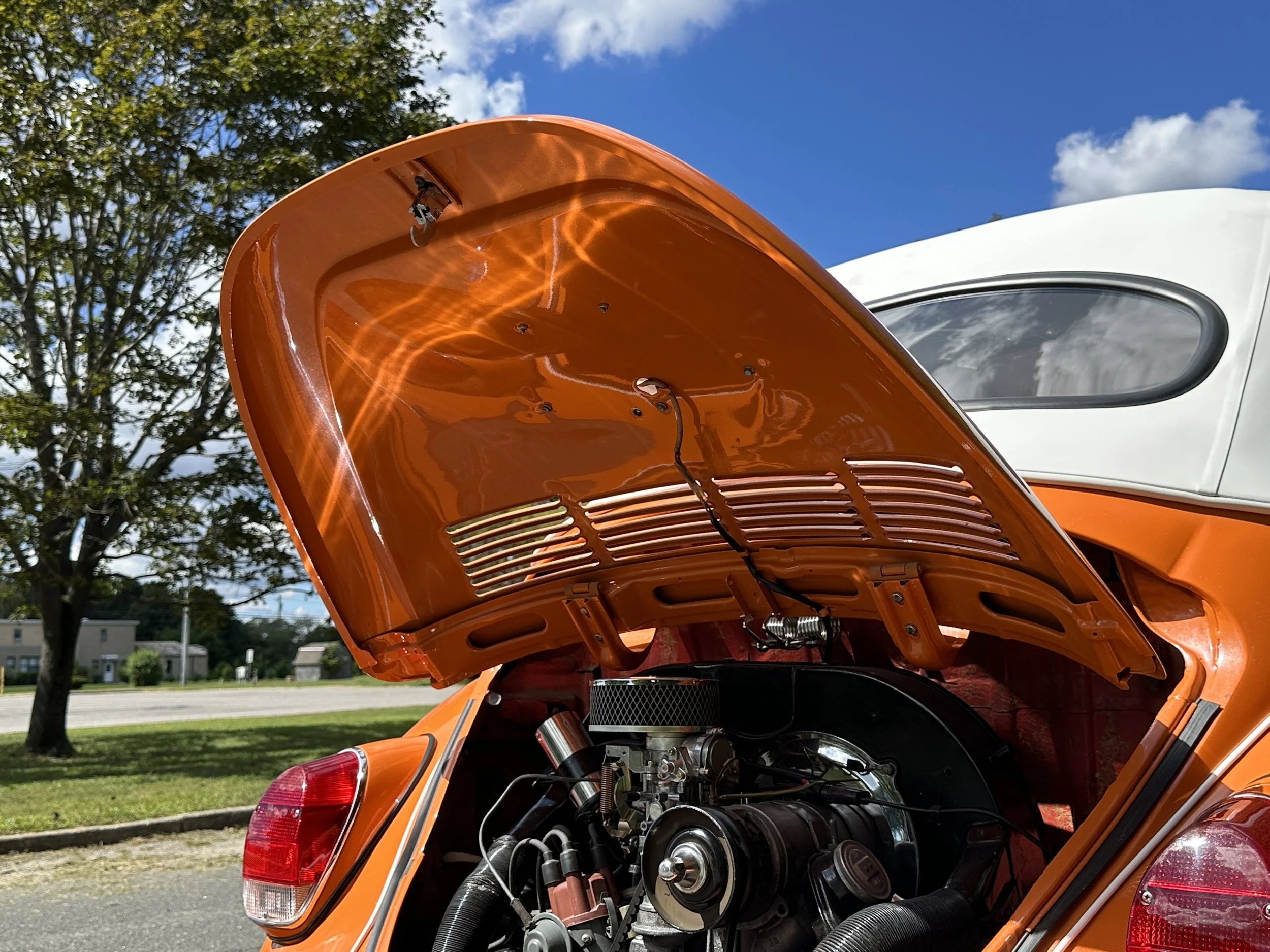 Close-up of the open hood of an orange classic Volkswagen Beetle showing its engine.