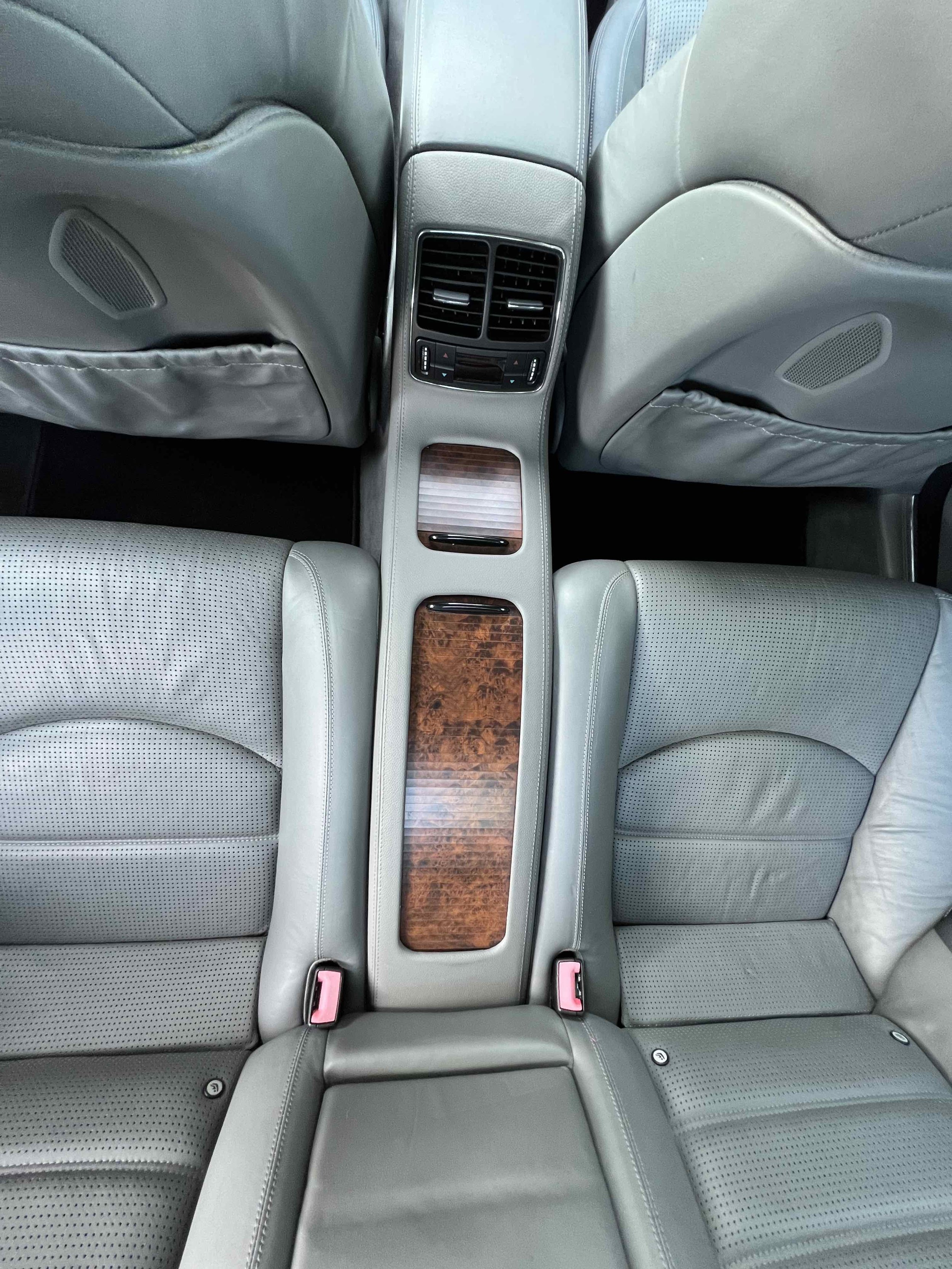 View of the back seats and center console of a car interior, featuring light gray leather seats, wood trim, and rear air conditioning vents.