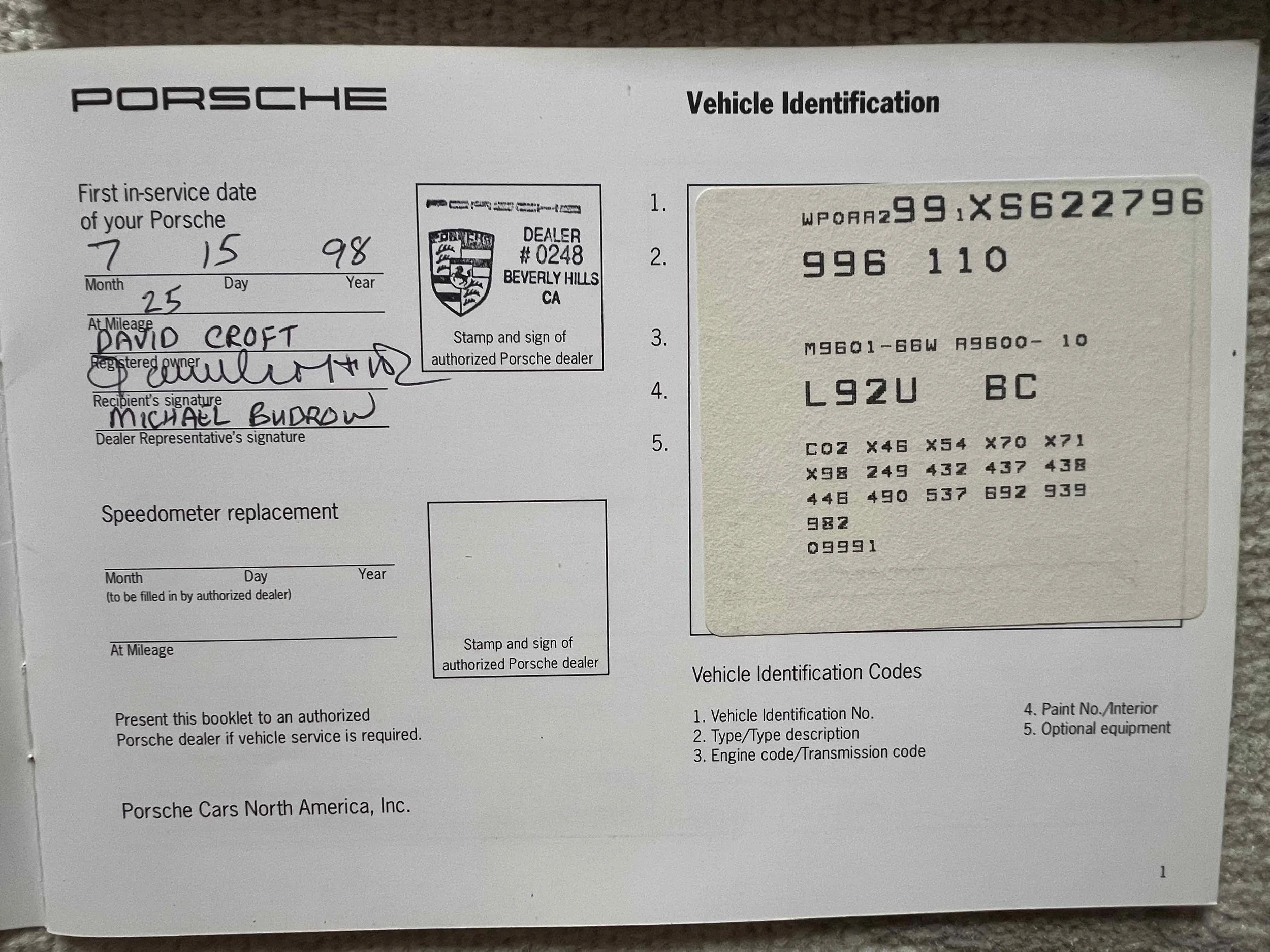 Porsche vehicle identification and service record document with handwritten details, including first in-service date, owner's name, and signatures, along with a sticker from an authorized Porsche dealer.