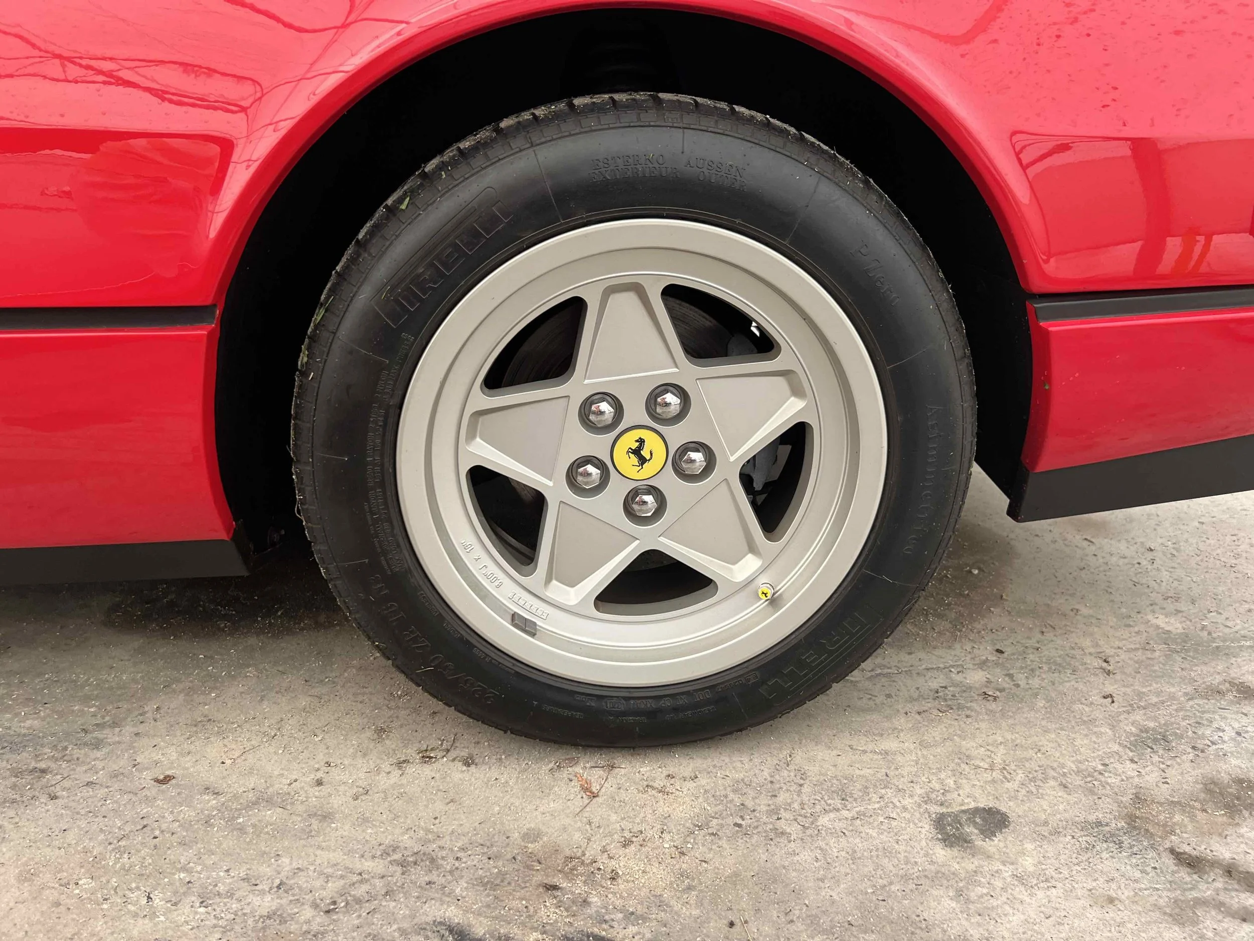 Close-up of a red sports car wheel with a silver alloy rim featuring the Ferrari logo in the center, and a black Pirelli tire.