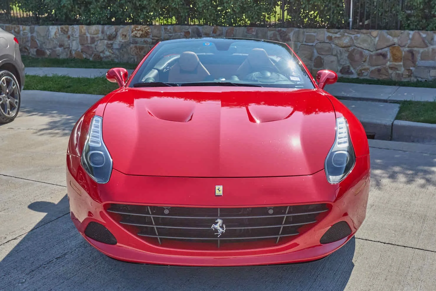 Front view of a red Ferrari convertible sports car parked on a concrete driveway.