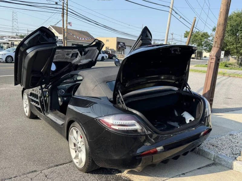 Black convertible sports car with its doors and trunk open parked on a street.