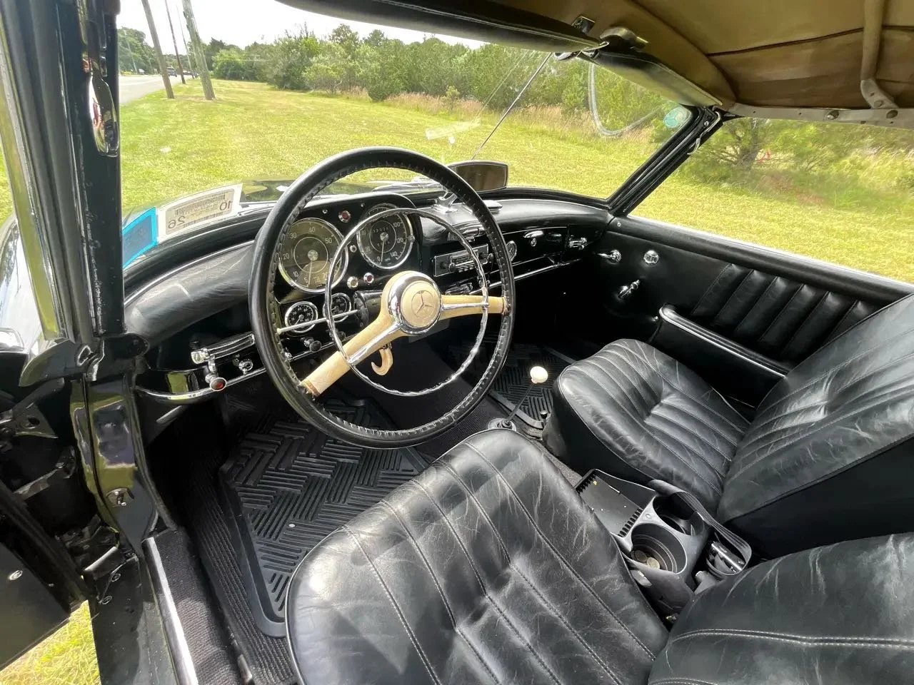 Interior of a vintage Mercedes-Benz car showing black leather seats, a black dashboard, a steering wheel with the Mercedes-Benz logo, and classic gauges.
