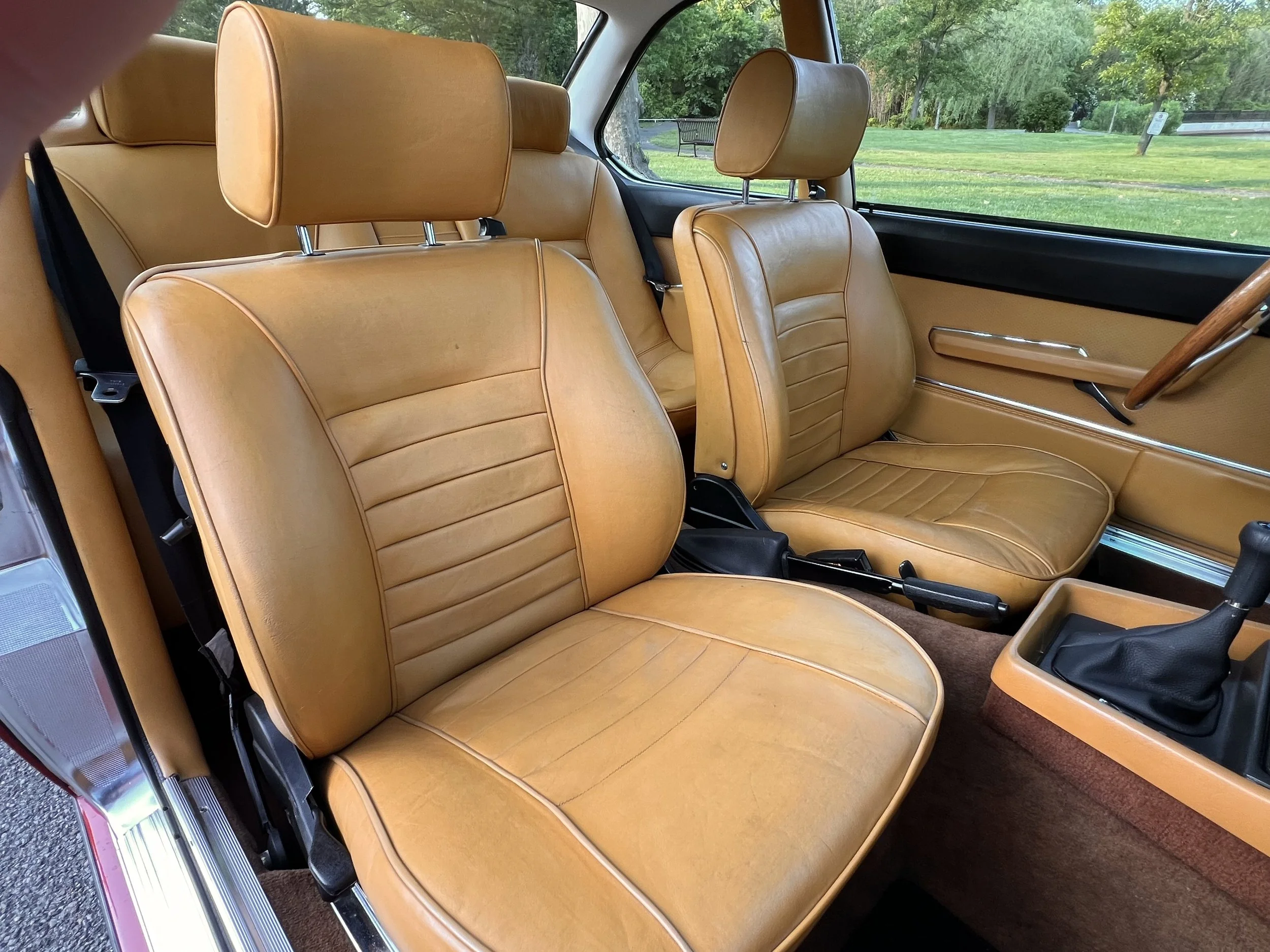 Inside of a vintage BMW 630 csi car showing tan leather seats, brown carpeting, and a gear shift.