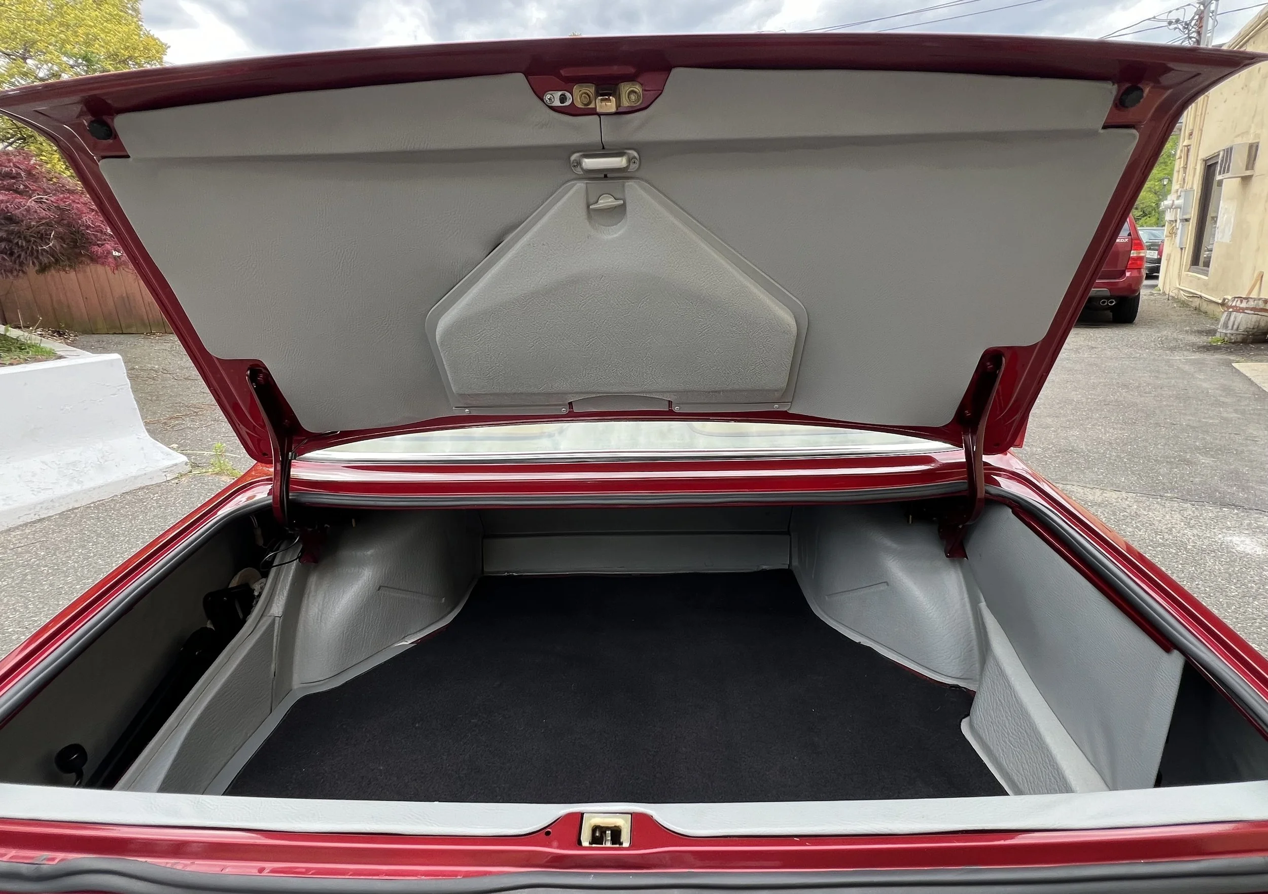 The open trunk of a red vintage 1977 BMW 630 csi car with gray interior lining and a black carpeted floor.