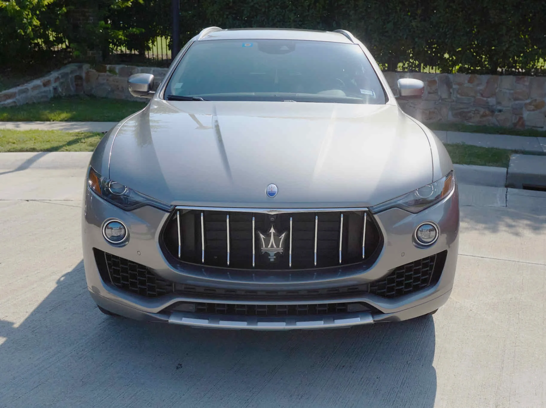 Front view of a silver Maserati SUV parked on a concrete surface with a stone wall and green bushes in the background.