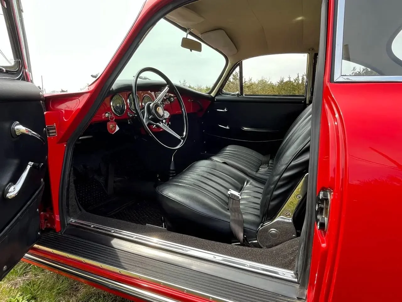 Interior of a vintage red car showing black leather seats, a red dashboard with gauges, and a steering wheel.