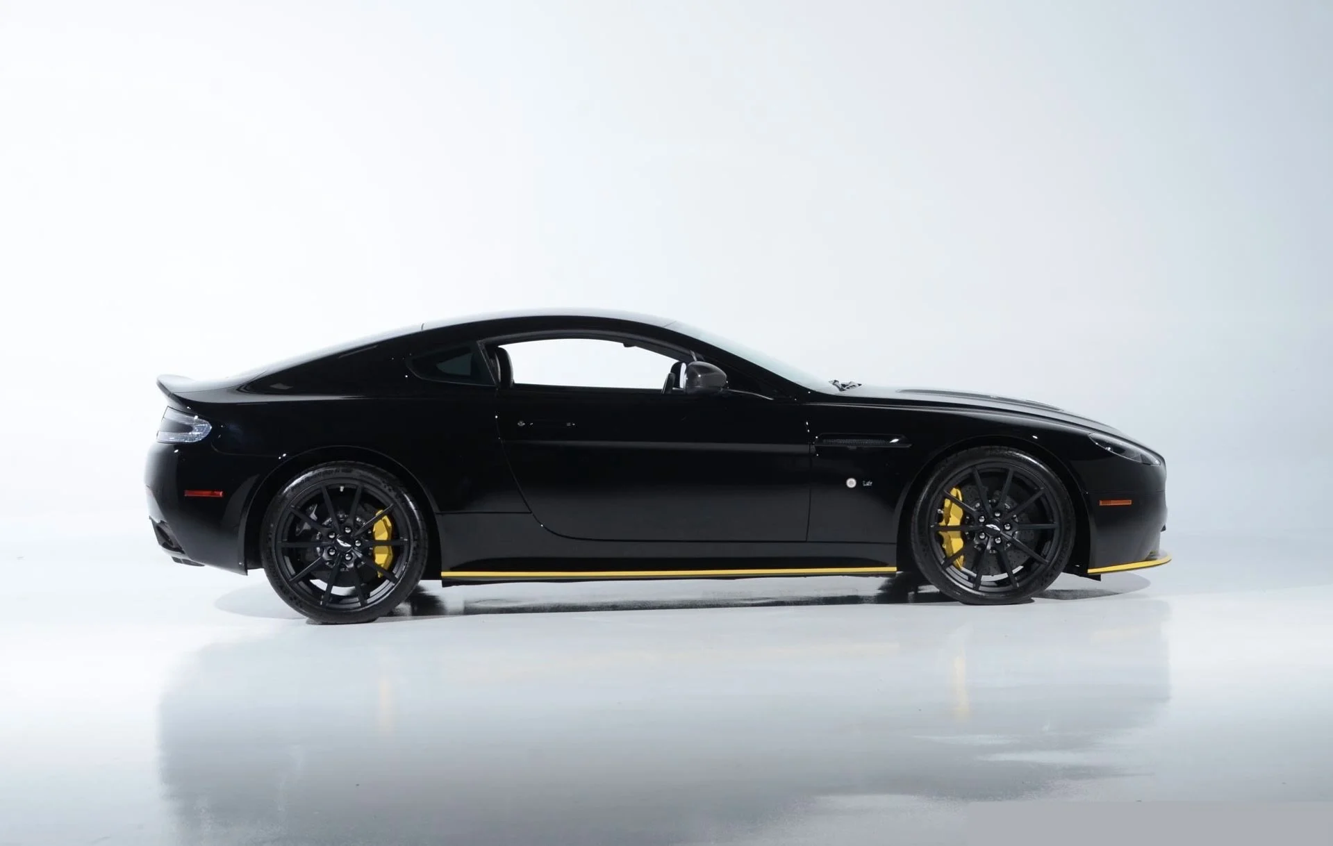 Side view of a sleek black sports car with yellow brake calipers and accents, set against a plain white background.