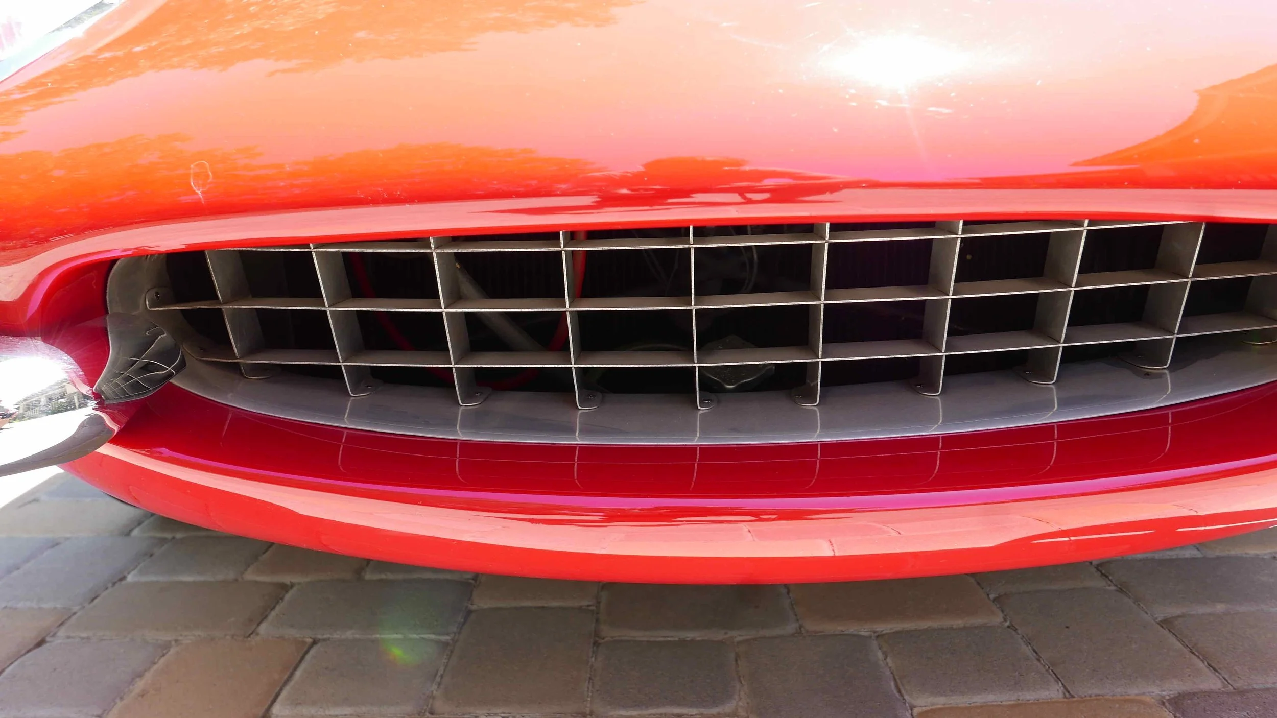 Close-up of the front grille of a red sports car, showing a horizontal and vertical grid pattern.