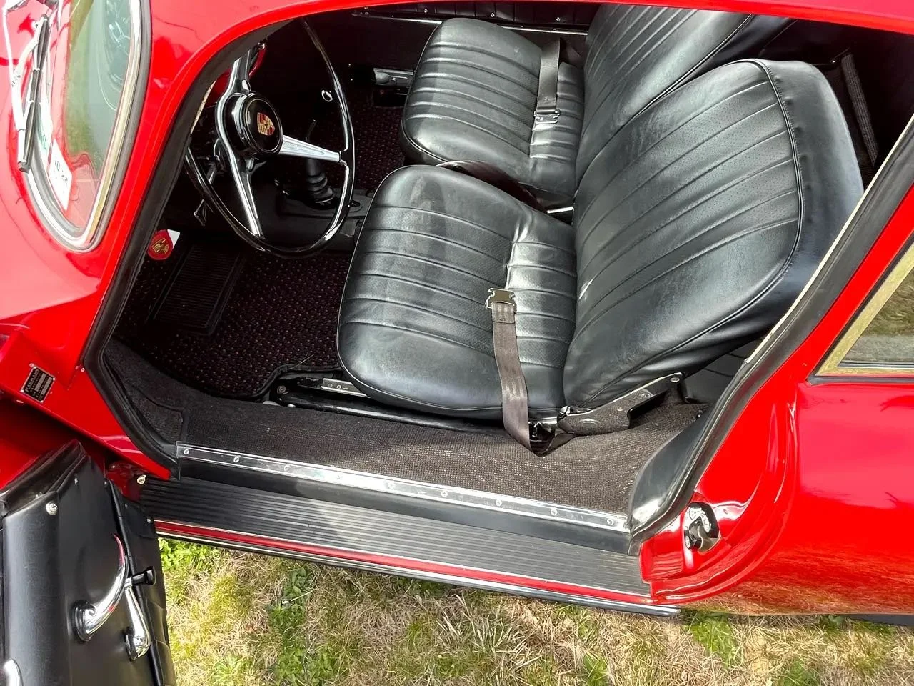 Interior of a vintage red car showing black leather seats, a black steering wheel with the Porsche emblem, and a glimpse of the driver's side door.