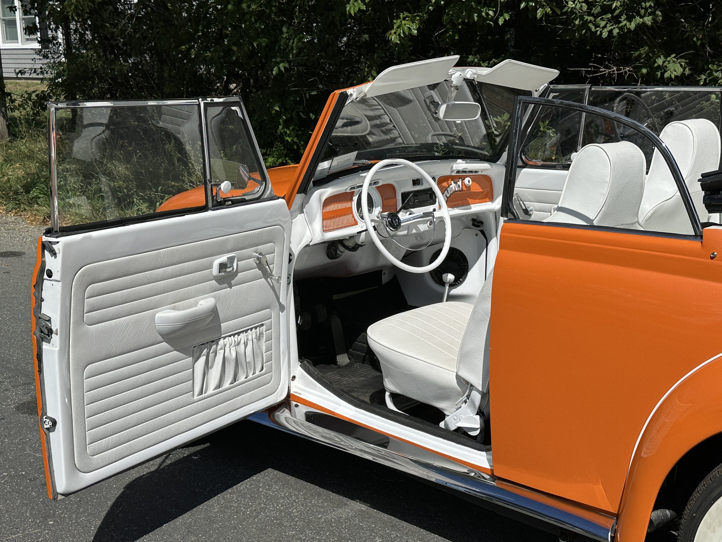Interior of a vintage orange and white convertible car with white seats, opened doors, and a white steering wheel.