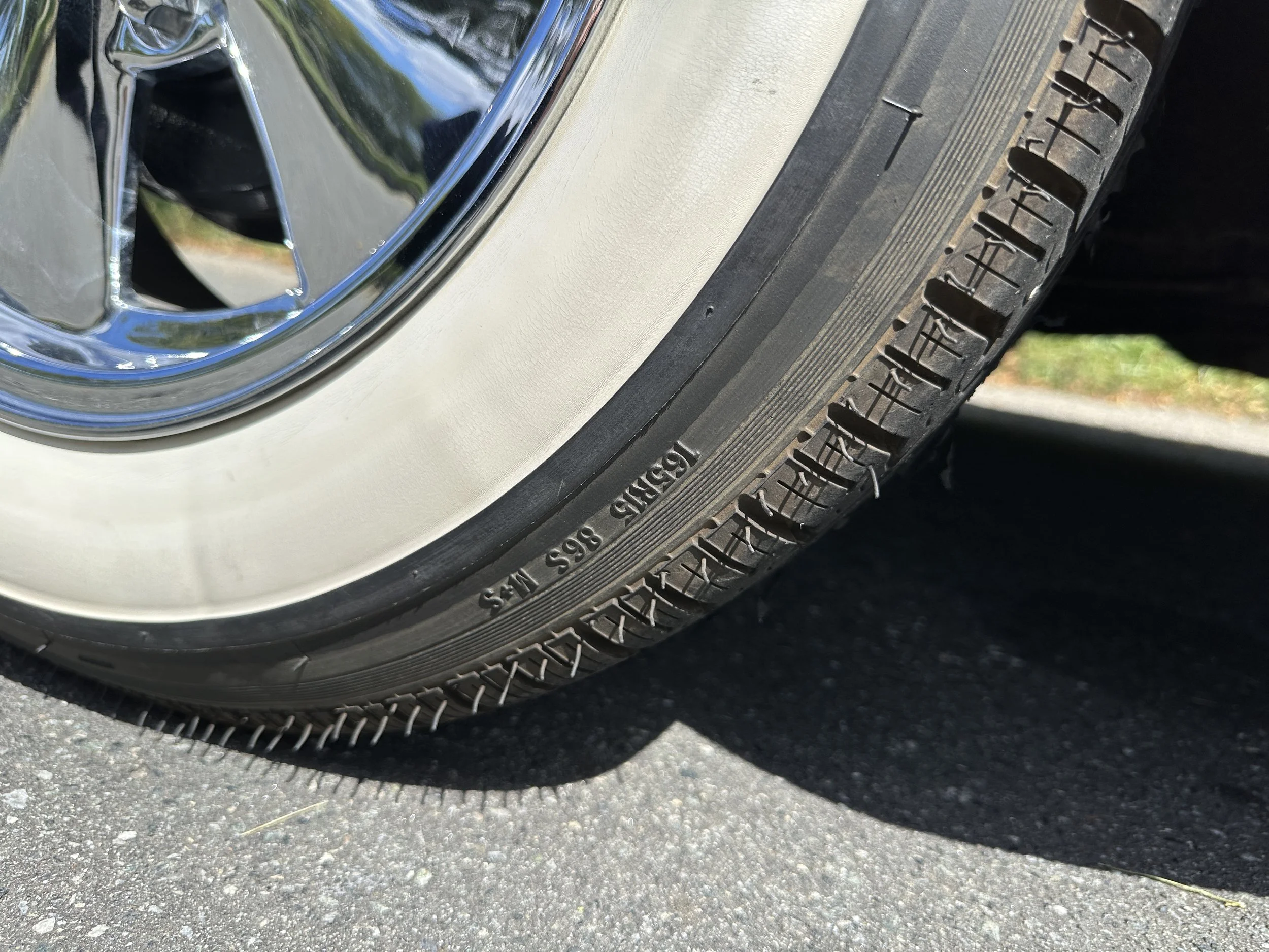 Close-up of a tire and chrome wheel on a vehicle parked on pavement, showing tread pattern and sidewall details.