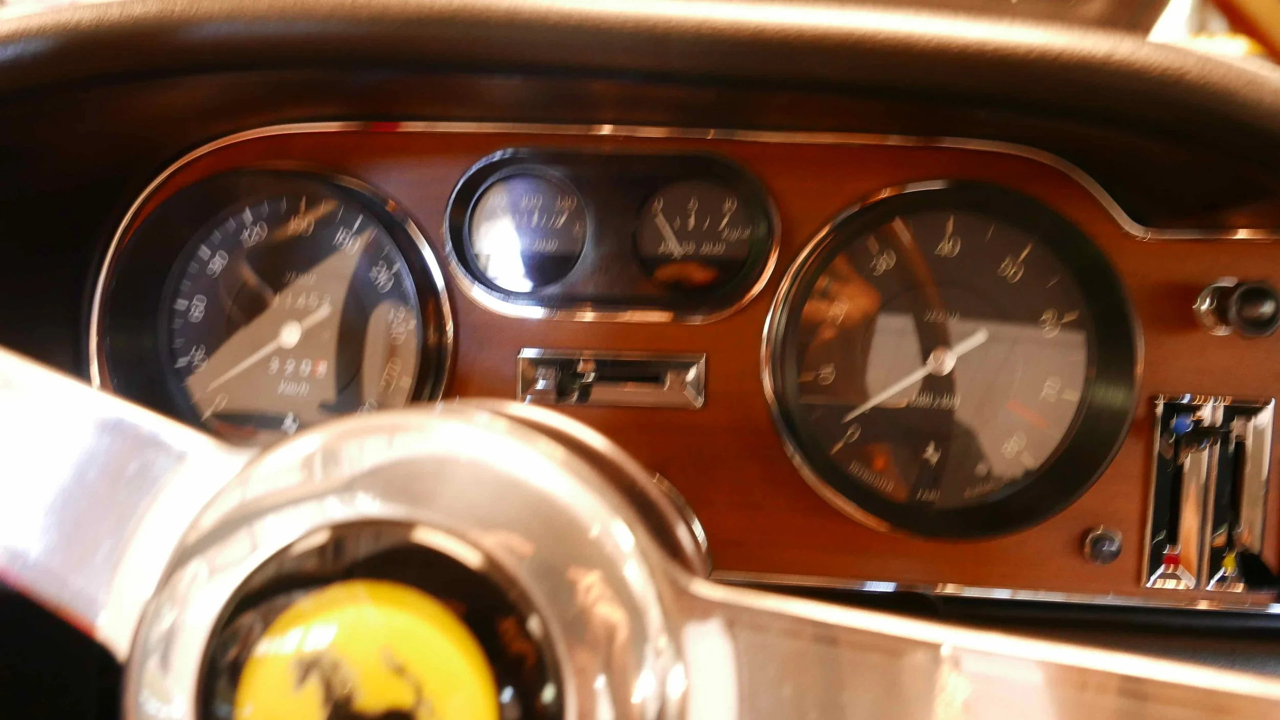 Dashboard of a vintage Ferrari with analog speedometer, tachometer, fuel gauge, and temperature gauge, with a steering wheel and gear shift.