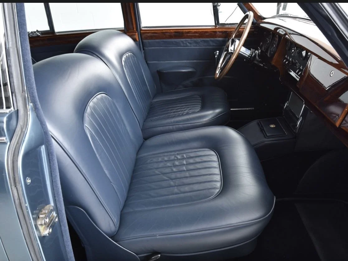 Interior of a vintage car with dark leather seats, wooden dashboard, and steering wheel.