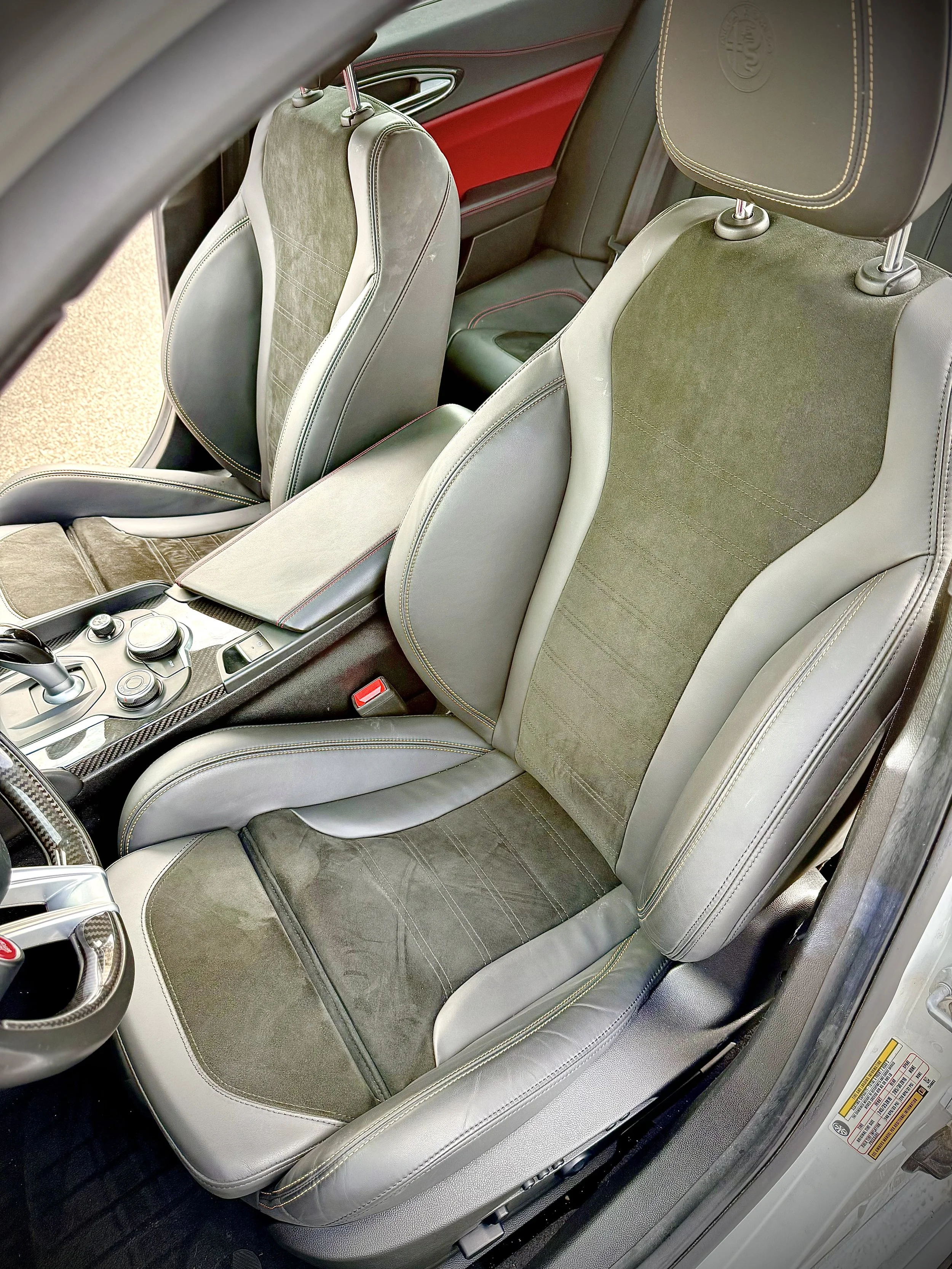 The interior of a sports car showing two front driver and passenger seats with gray leather and green suede inserts, dashboard, and center console.