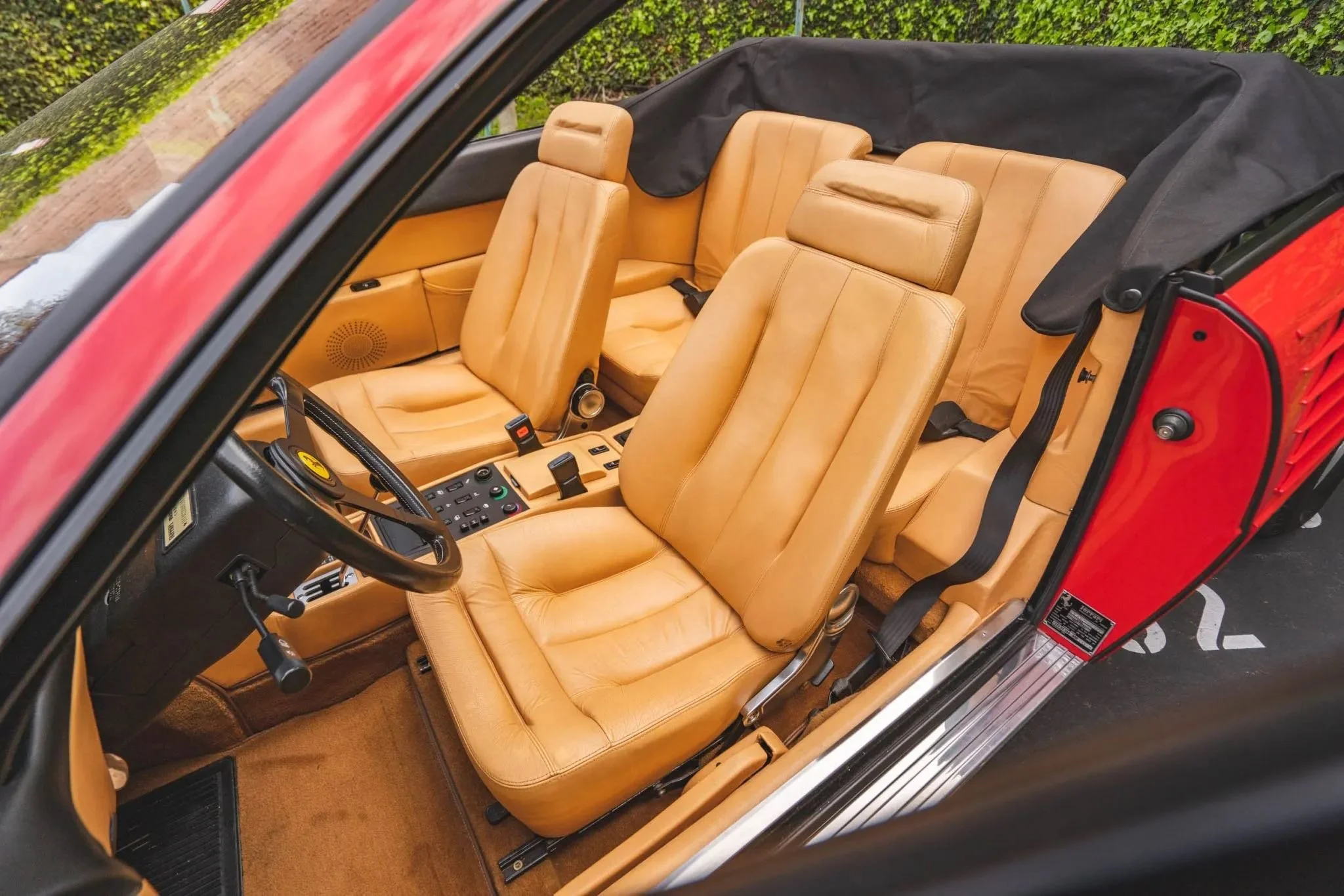 Interior of a vintage car with tan leather seats, a black steering wheel, and a dashboard with various controls, photographed from above.
