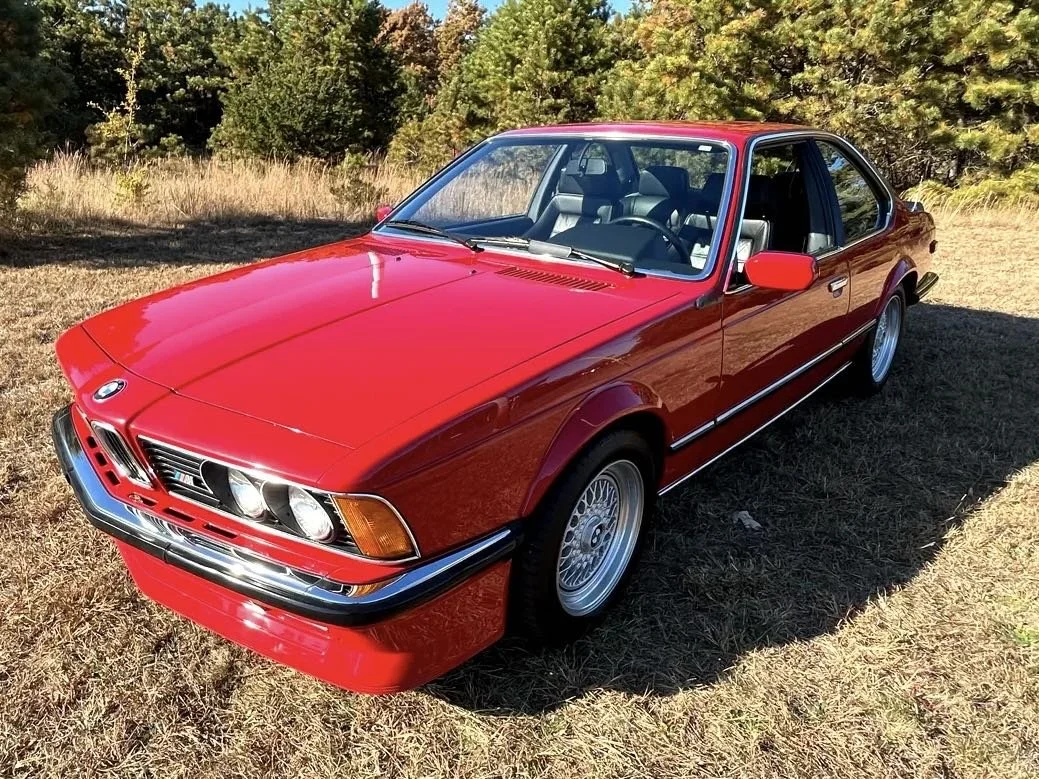 A red classic BMW coupe parked on grass with trees in the background.