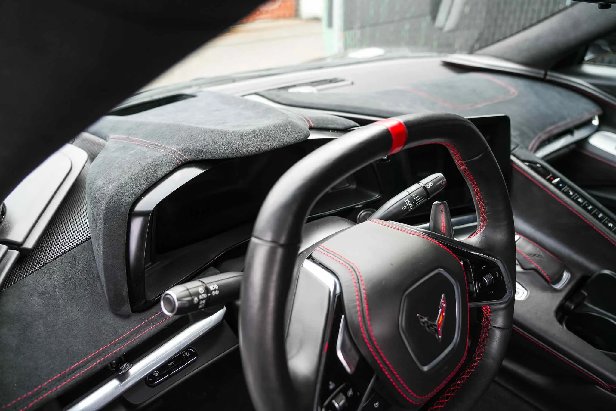 Inside view of a sports car dashboard, steering wheel with red stitching, and dashboard controls with red accents.