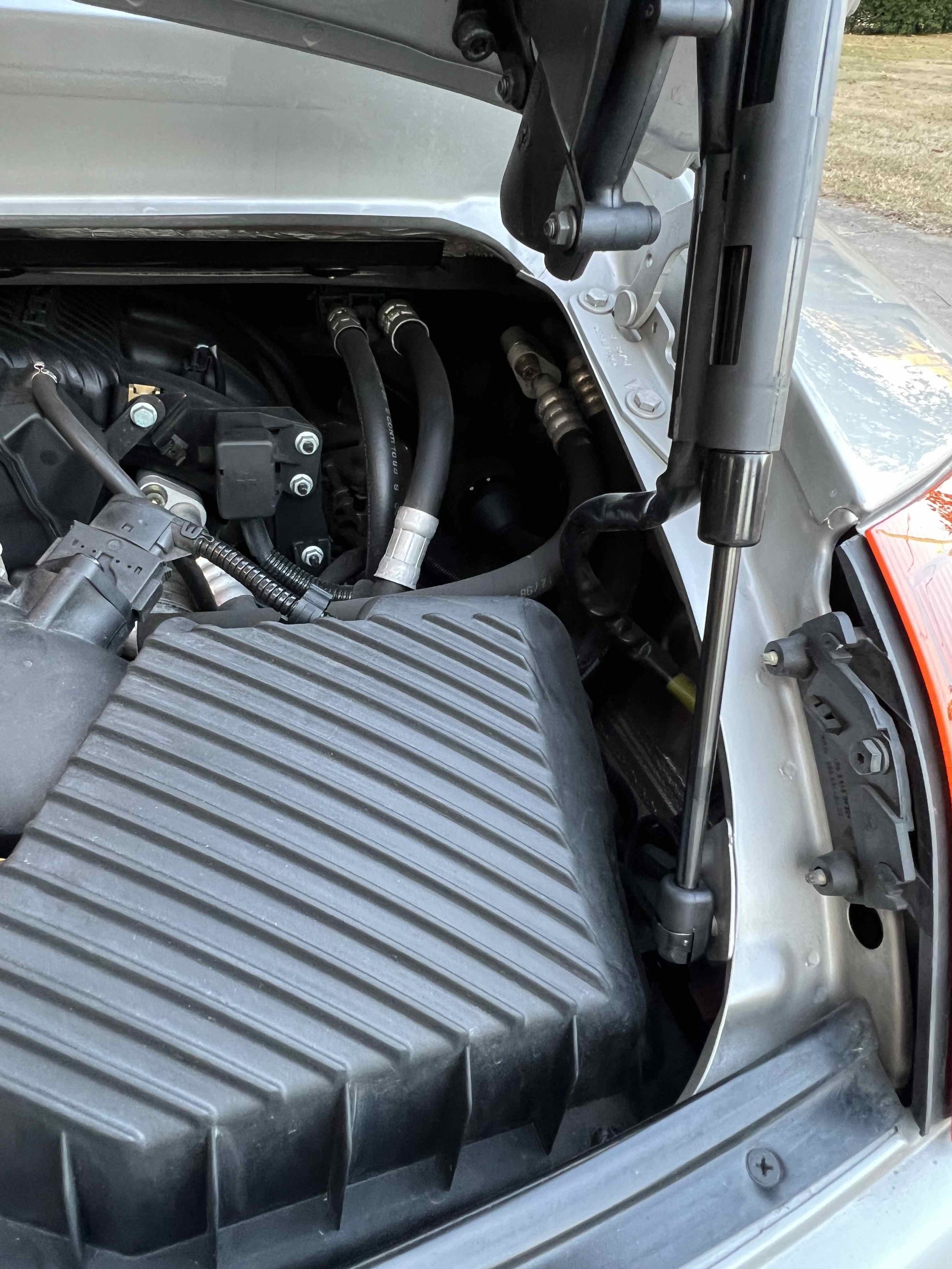 Close-up of a car engine with visible hoses, wiring, and engine components under the hood.