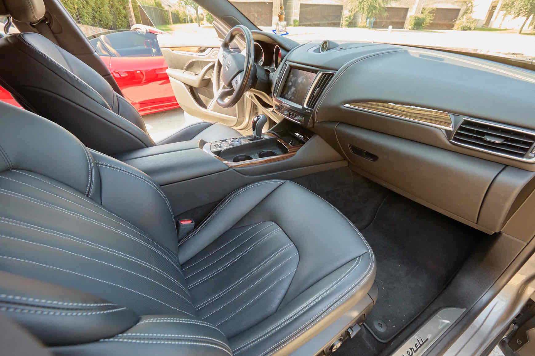 Interior of a car showing black leather seats with white stitching, a dashboard with a large touchscreen display, and a gear shift in the center console.