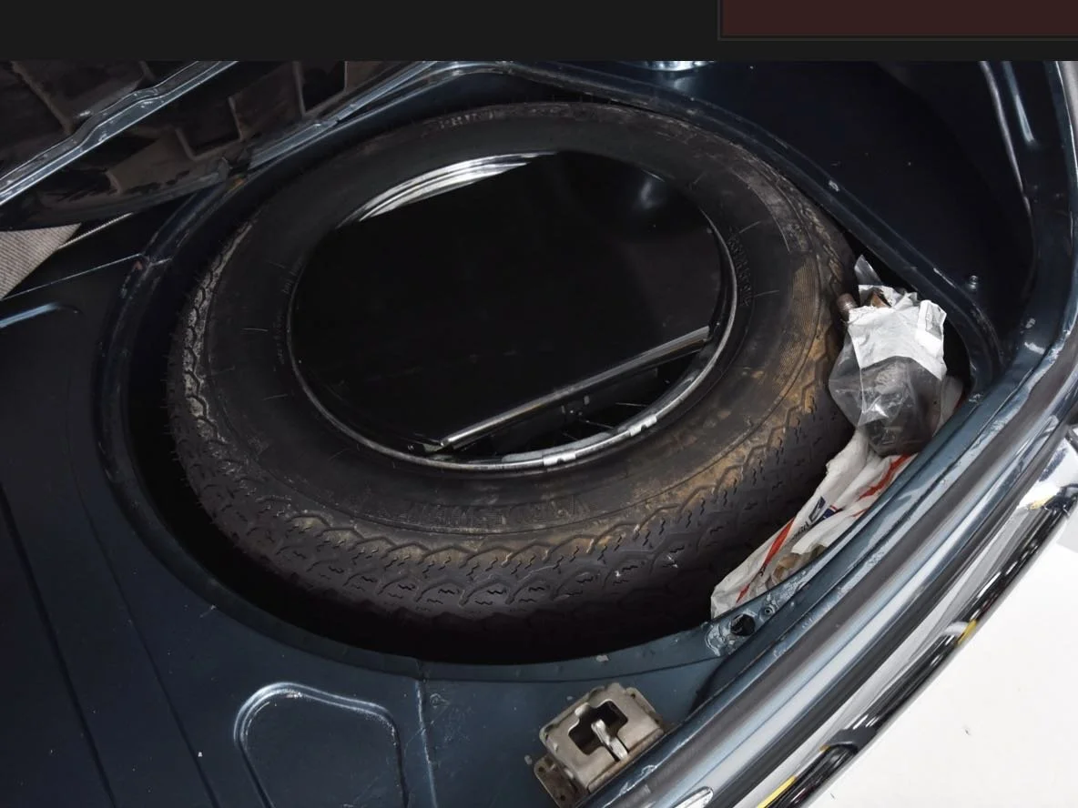 Open car trunk with spare tire inside, along with some plastic bags and tools.