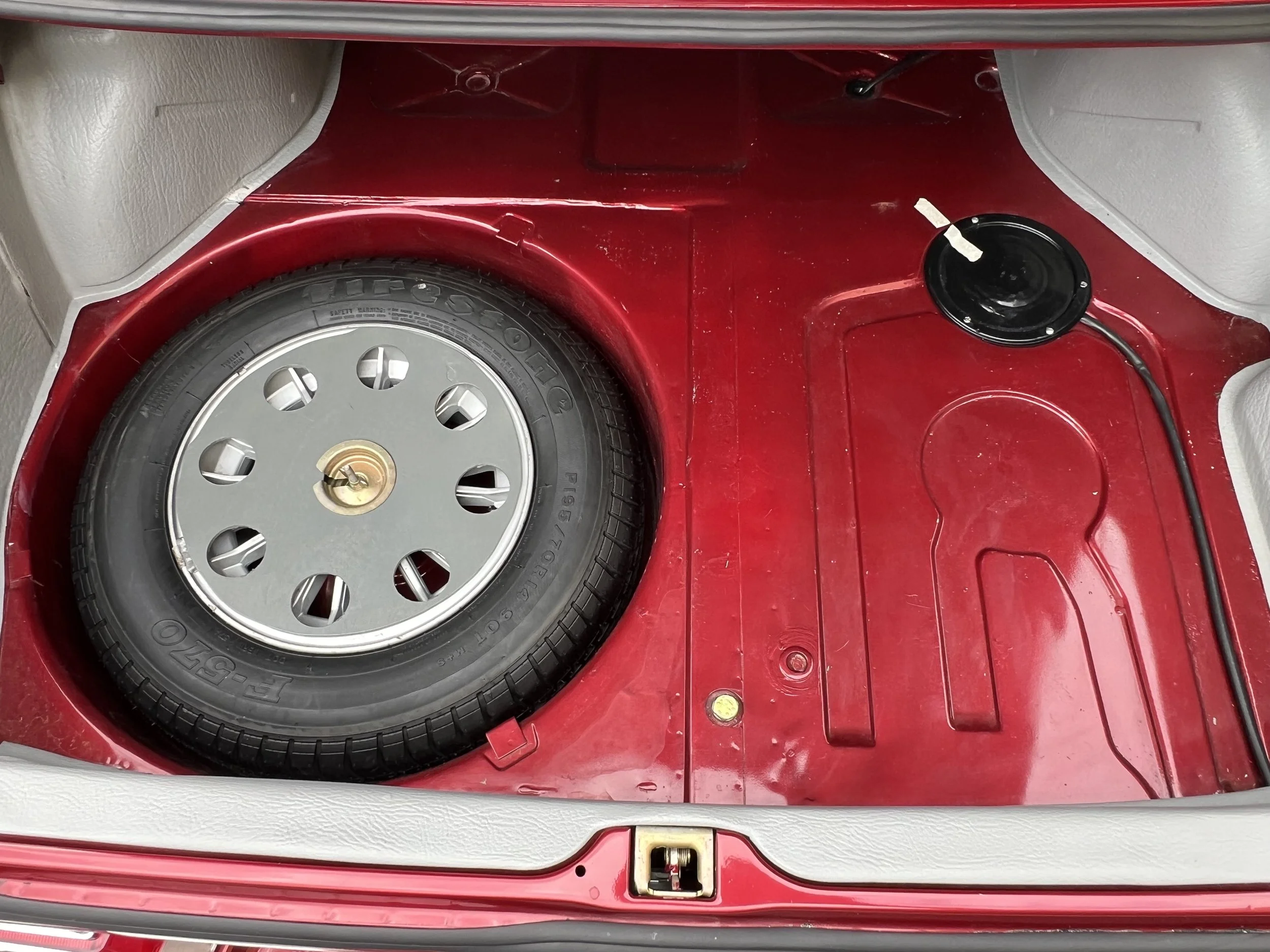 Spare tire in the trunk of a 1977 BMW 630 csi car, with a black speaker nearby and a red interior surface.