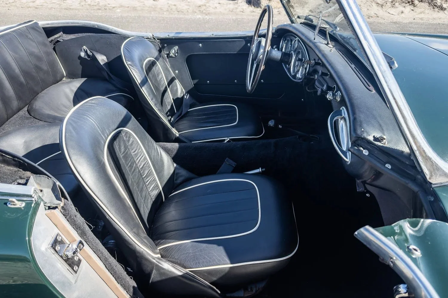 Interior of a vintage convertible car with black leather seats and a dashboard with gauges.