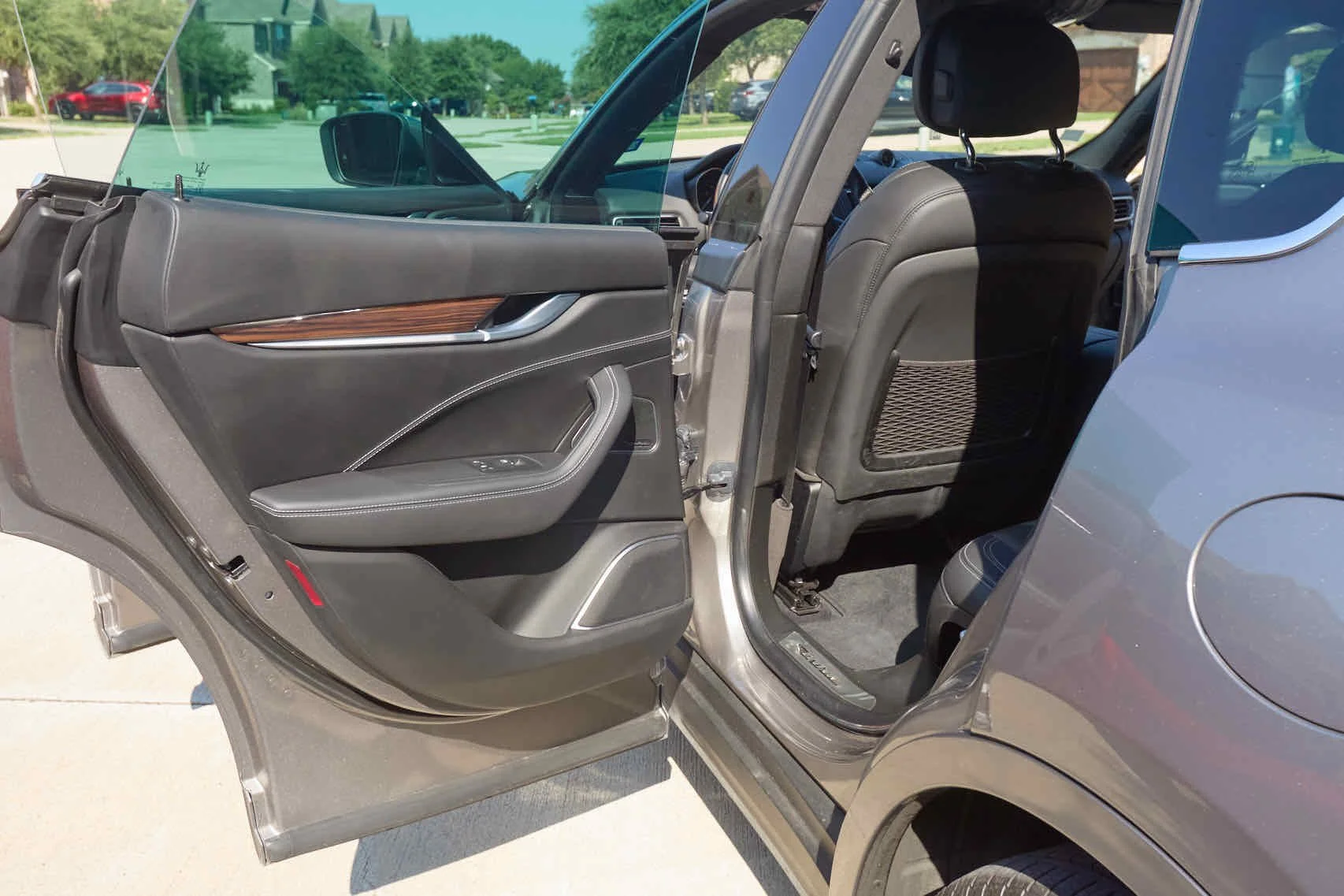 Open car door showing interior of a luxury vehicle with black leather seats and wood trim, parked outdoors on a sunny day.