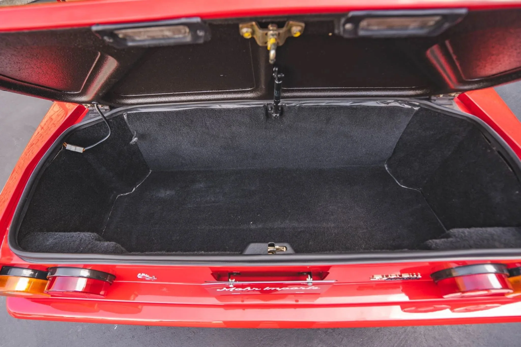 Open trunk of a red Porsche 911 with black carpet lining.