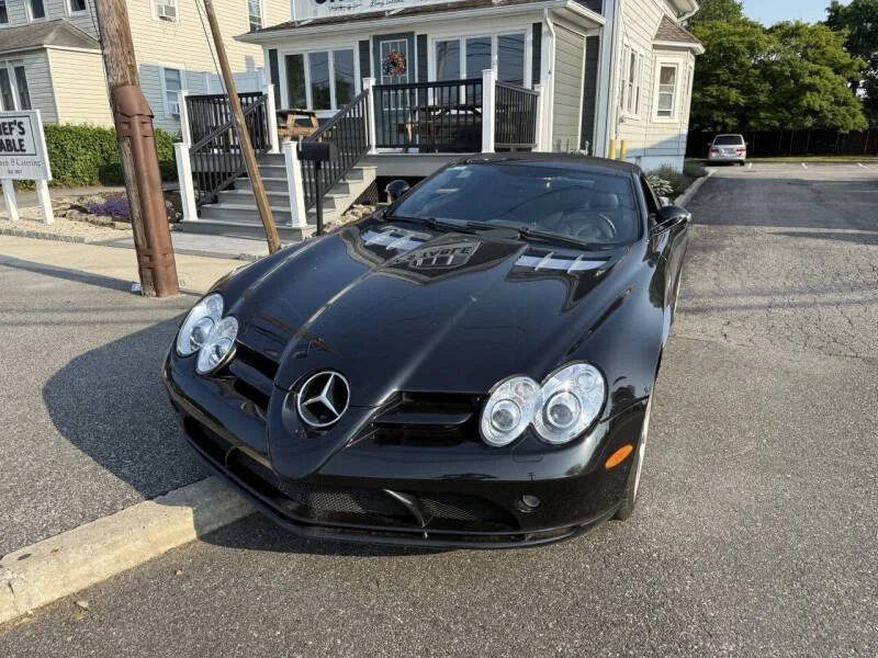 Black Mercedes-Benz sports car parked on a street in front of a house with a porch and stairs.