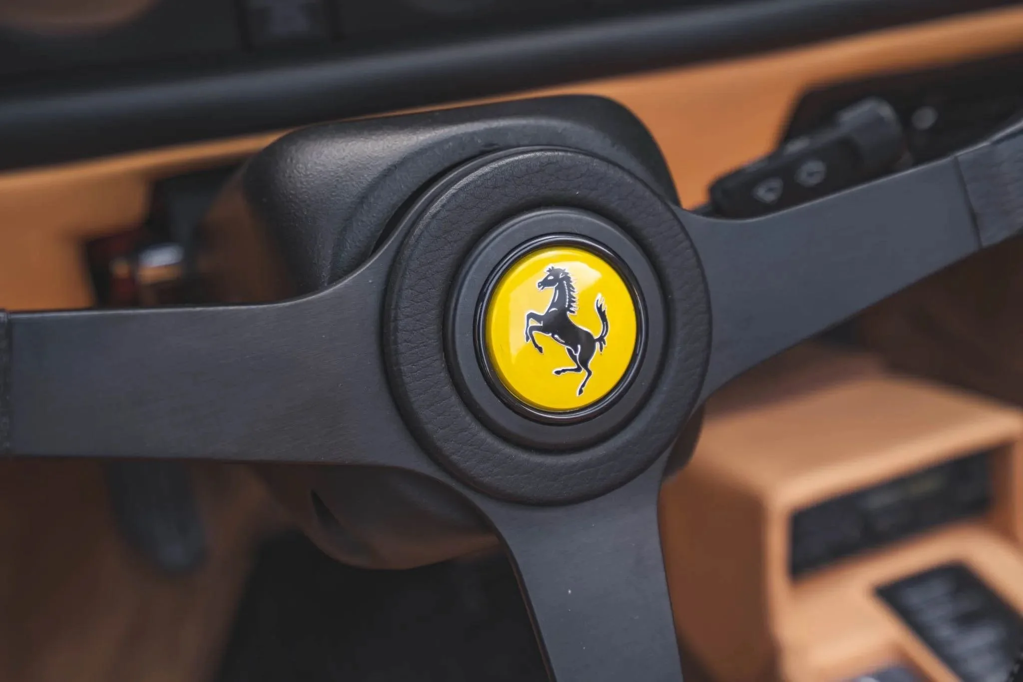 Close-up of a vintage Ferrari steering wheel with Ferrari logo in the center, showing a black prancing horse on a yellow background.