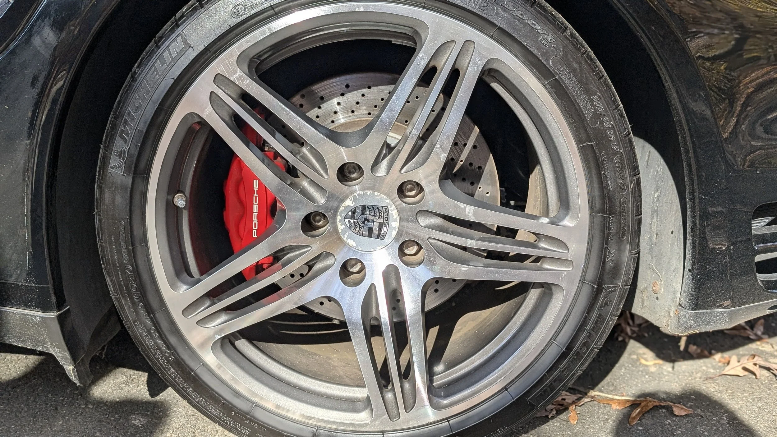 Close-up of a Porsche car wheel with a multi-spoke alloy rim, a red brake caliper, and a perforated brake disc.