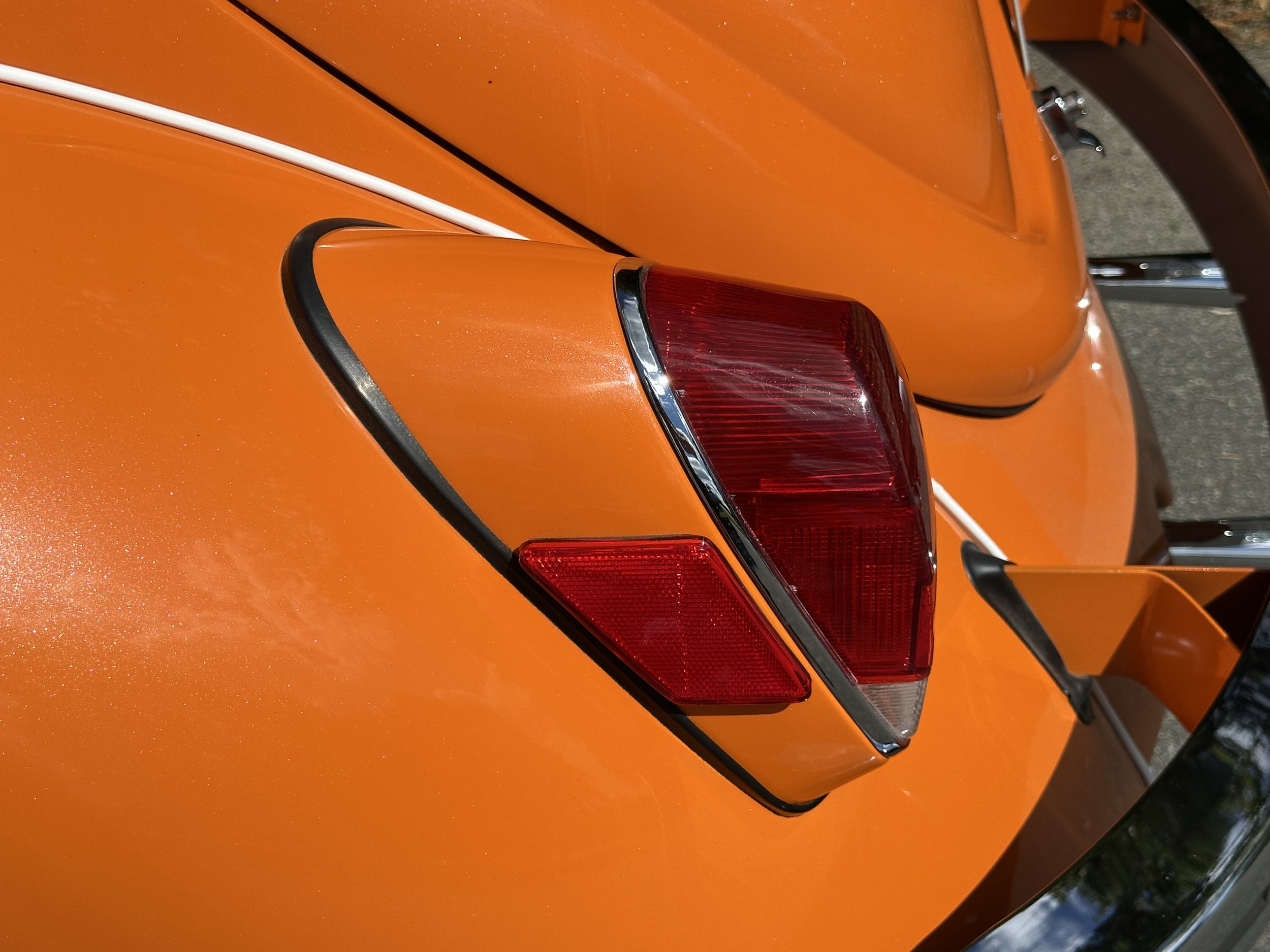 Close-up of the rear section of an orange vintage car, showing the taillight, black trim, and part of the rear spoiler.