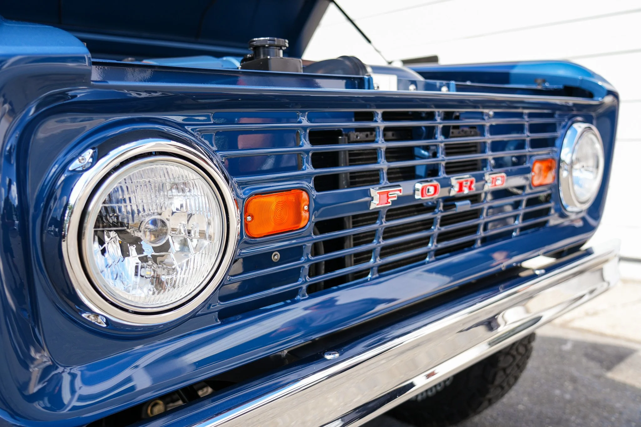 Close-up of a vintage blue Ford truck front grille with round headlights and orange turn signals, showcasing the Ford emblem.