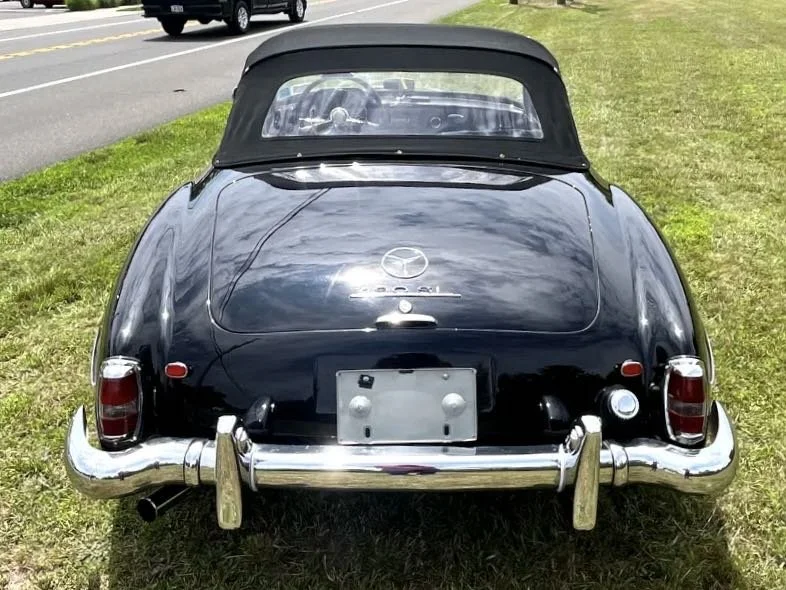 Black vintage Mazda convertible car parked on grass next to a road, with a silver bumper and a local registration plate.