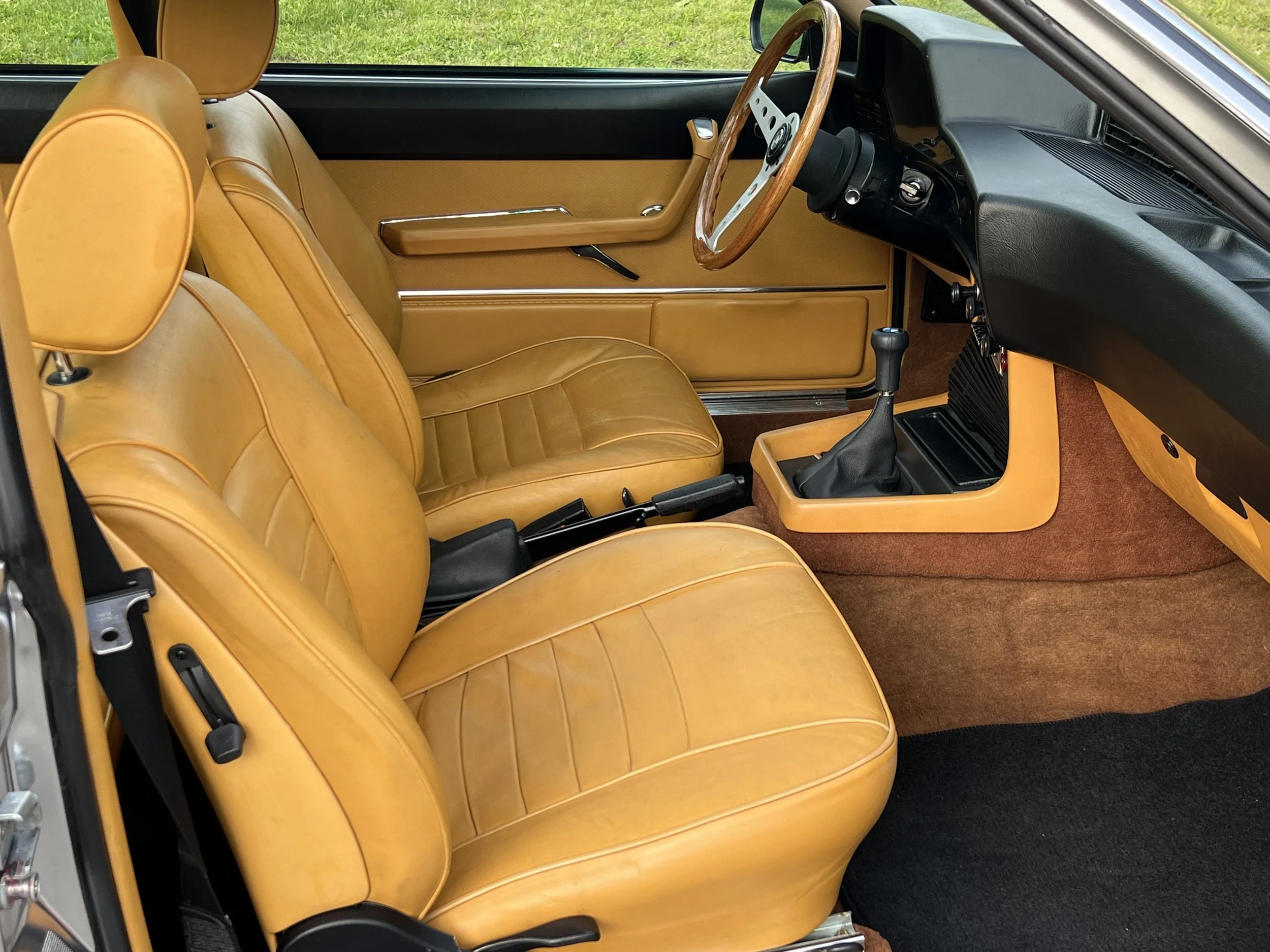 Interior of a vintage BMW 630 csi car with tan leather seats, wood steering wheel, and black dashboard.
