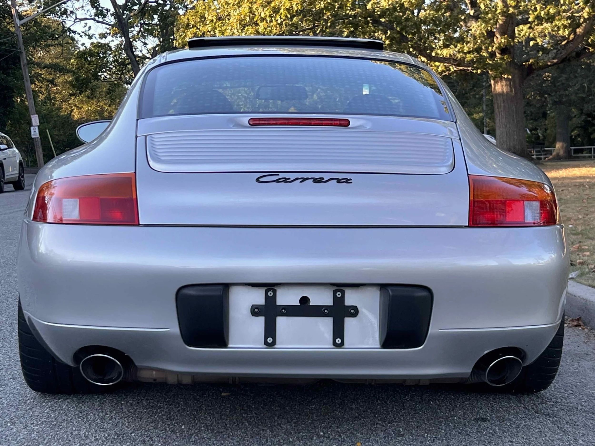Rear view of a silver Porsche Carrera parked on a street with trees in the background.