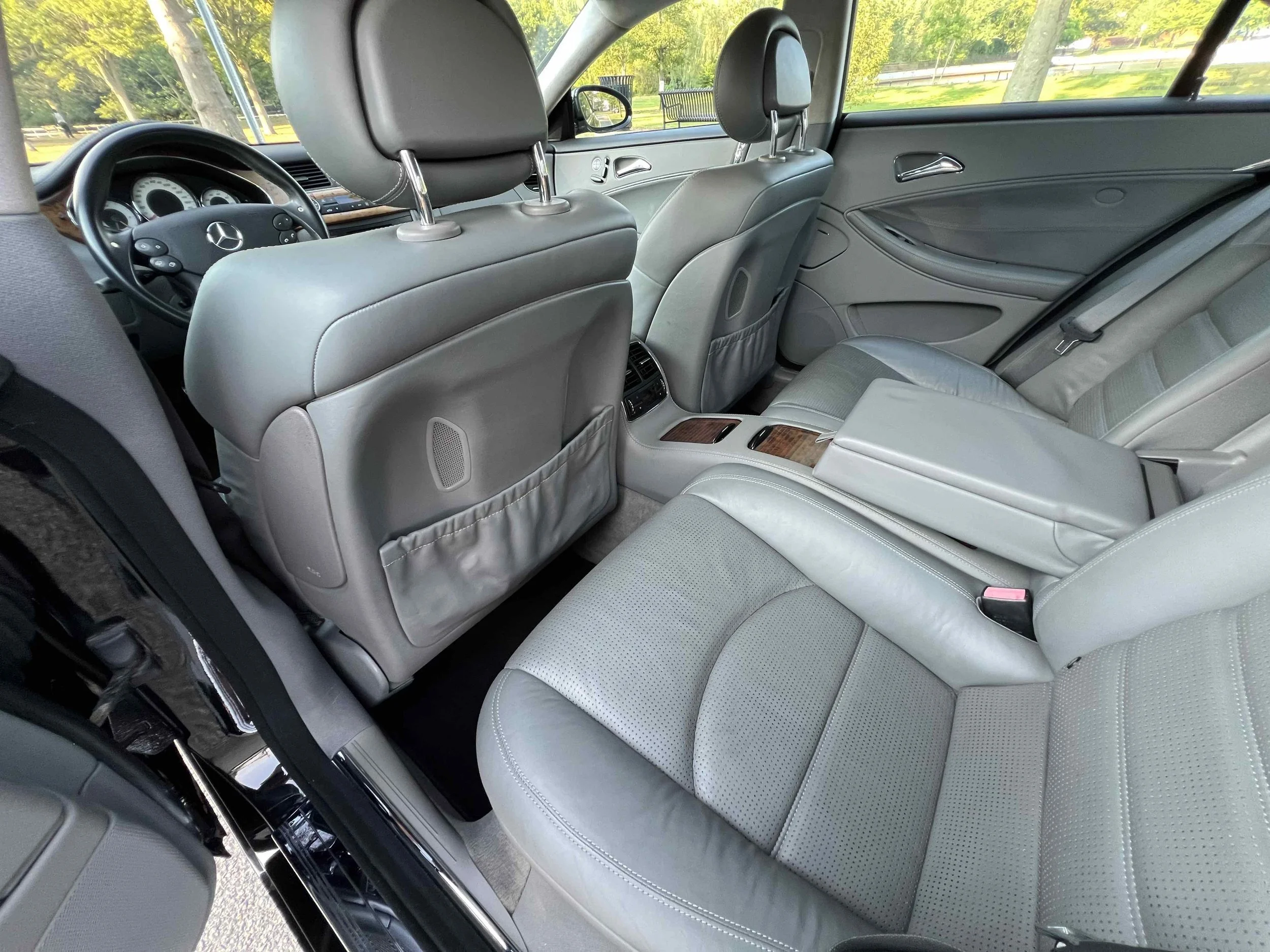 Interior of a luxury vehicle showing two front seats and the back seats with leather upholstery, wood trim accents, and a view of the dashboard and steering wheel through the front windshield.