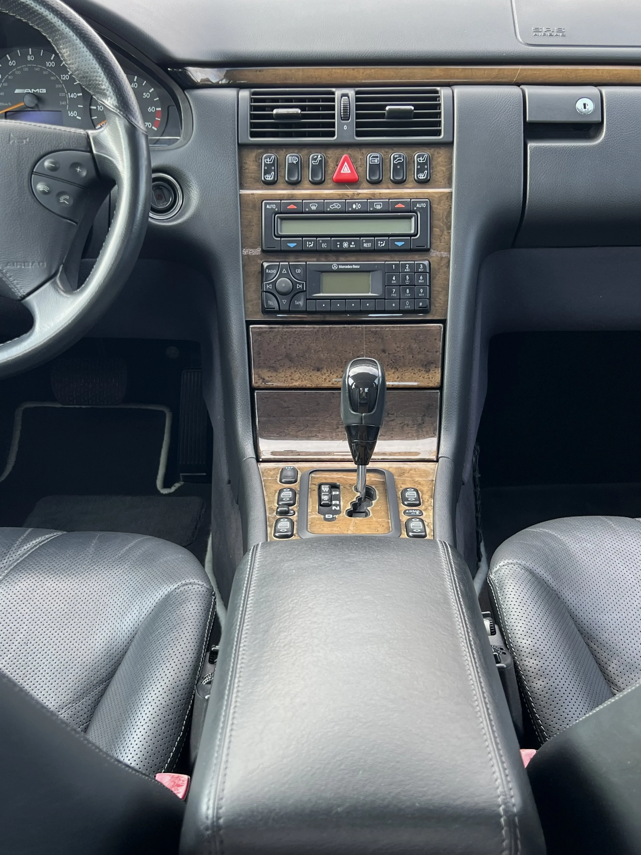 Interior view of a car showing the dashboard, steering wheel, leather seats, gear shift, and center console with control buttons and a digital display.