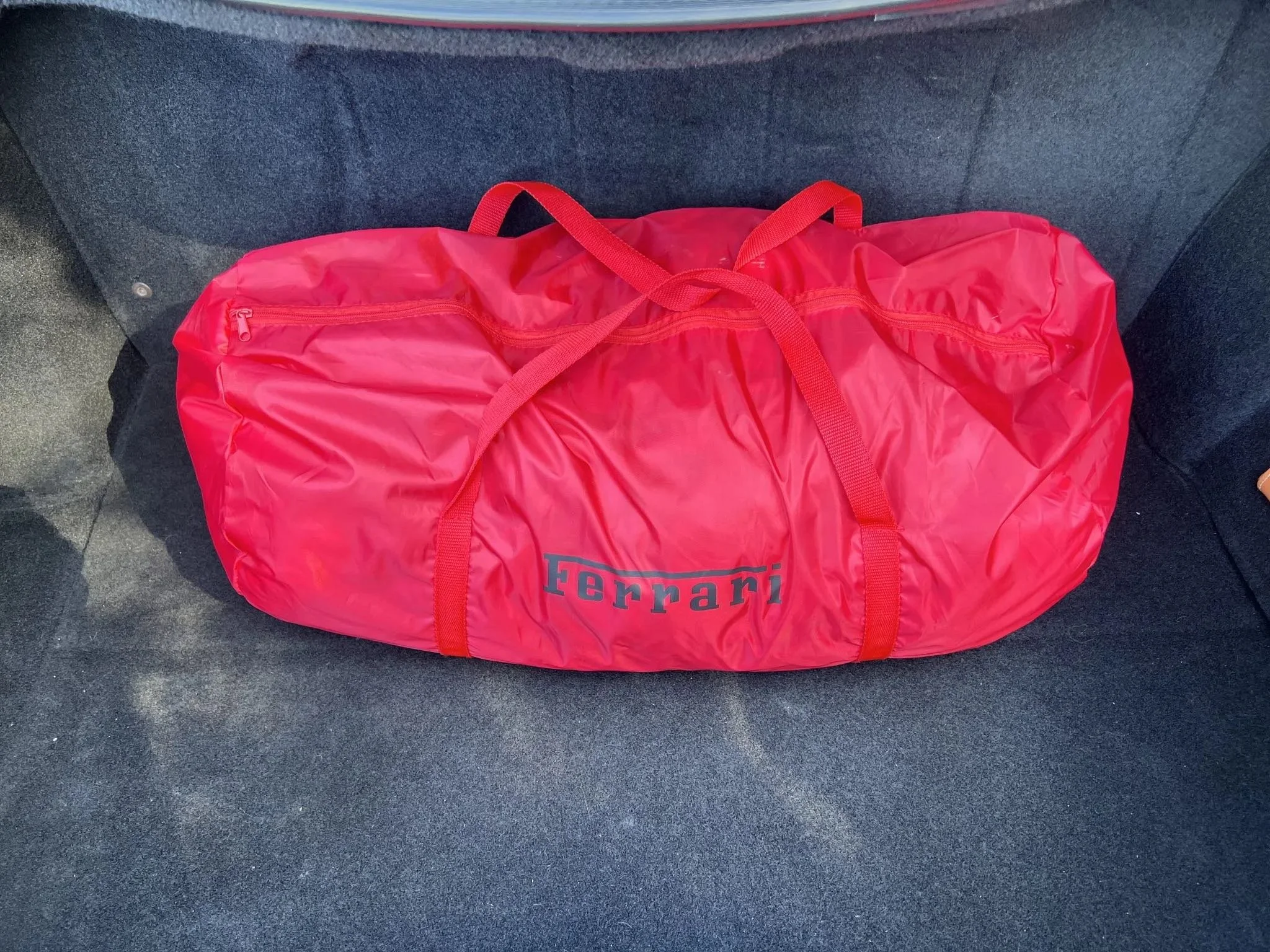 Red Ferrari branded duffel bag on dark gray car seat.