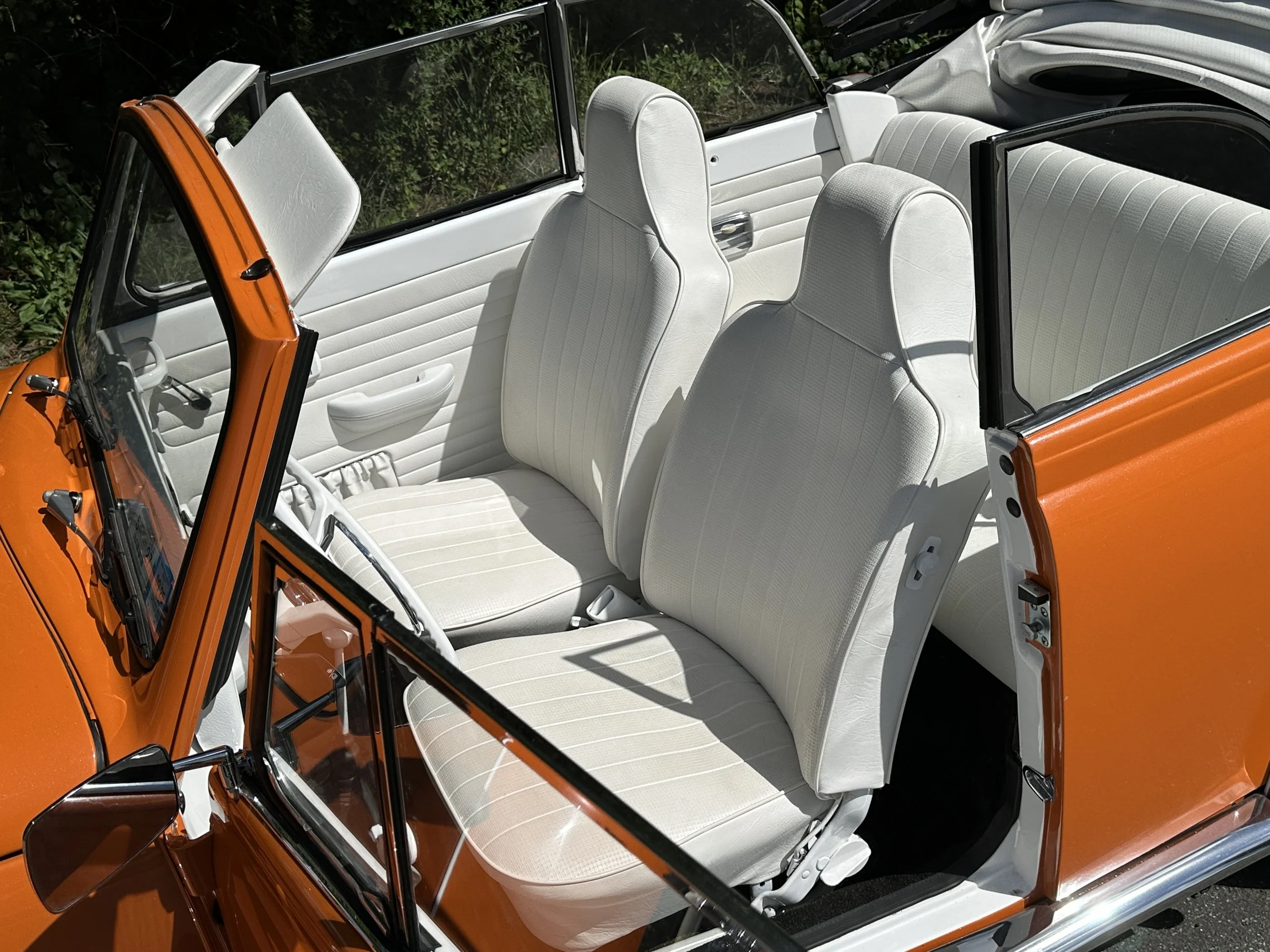 The interior of a vintage orange car with white seats and a black dashboard, viewed from above.