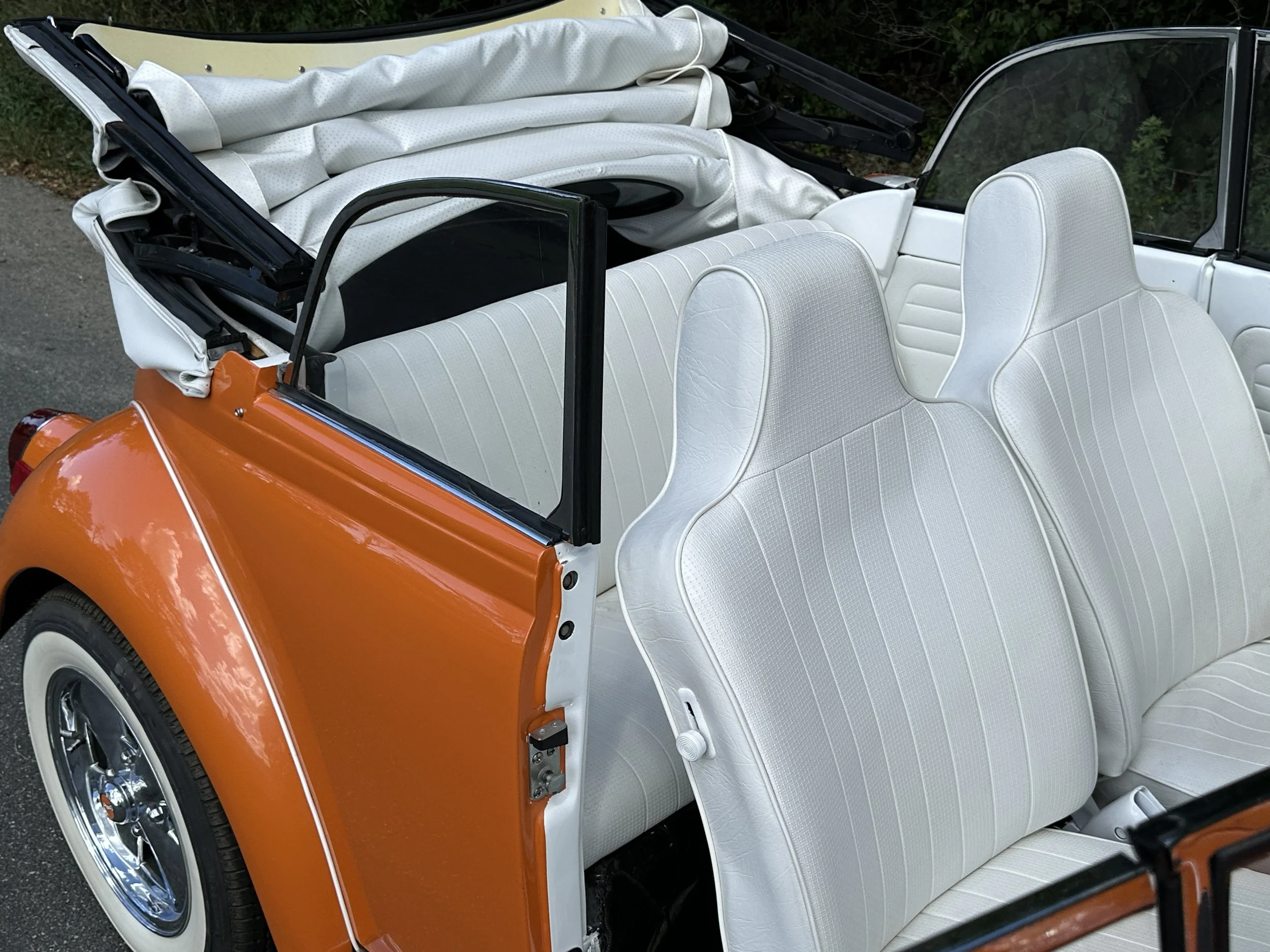 Close-up of a vintage orange convertible car with white seats and a lifted white soft-top roof.