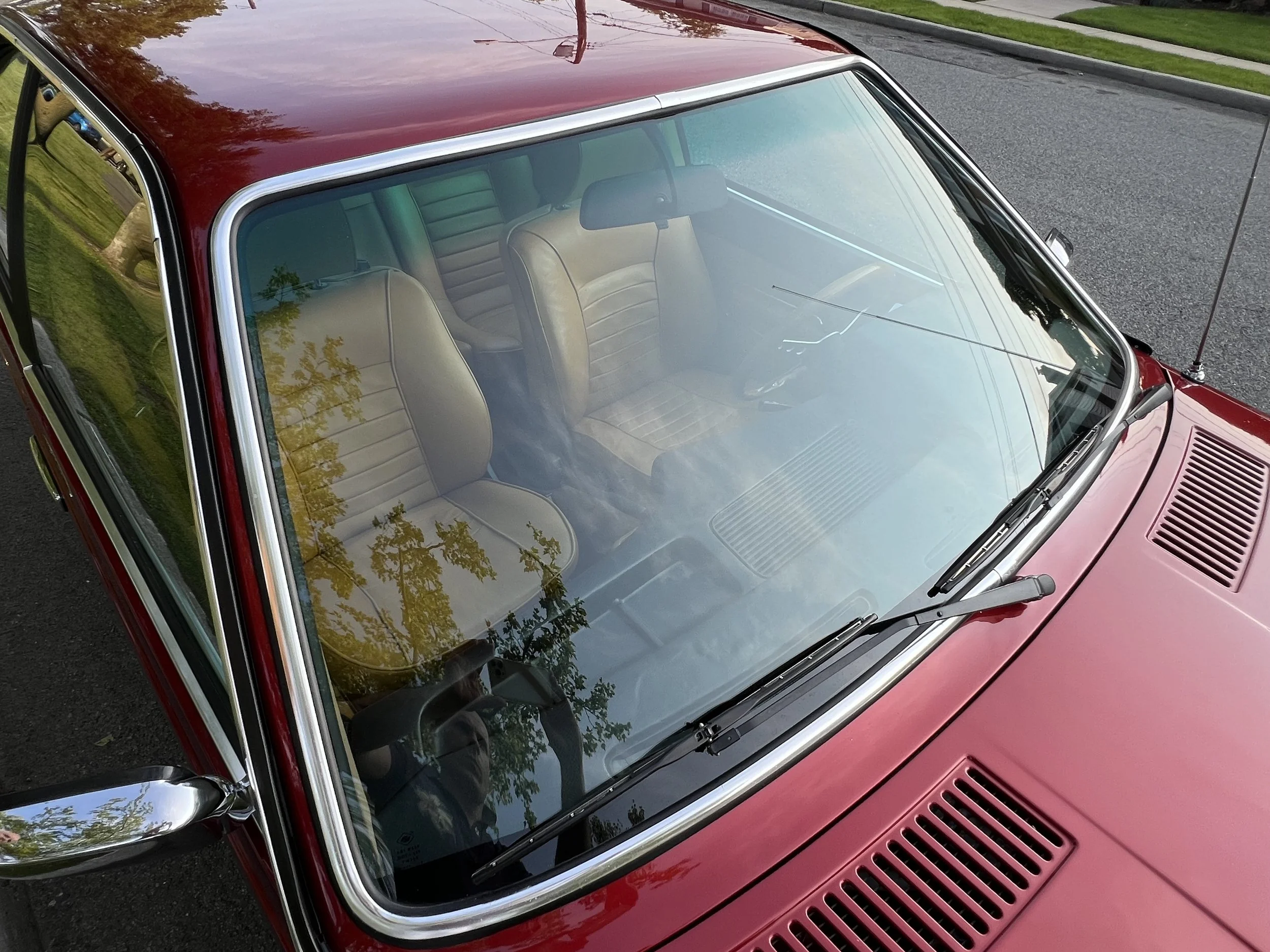 Red vintage BMW 630 csi front interior and windshield reflecting trees, showing beige seats and dashboard from above